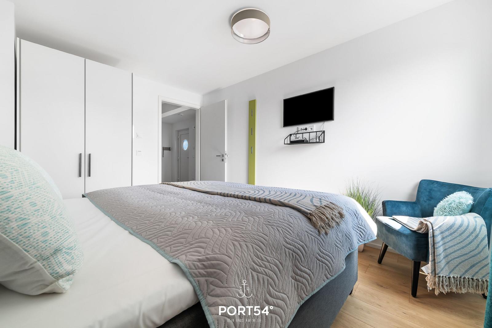 Schlafzimmer mit Bett, Kleiderschrank, TV und Sessel.
