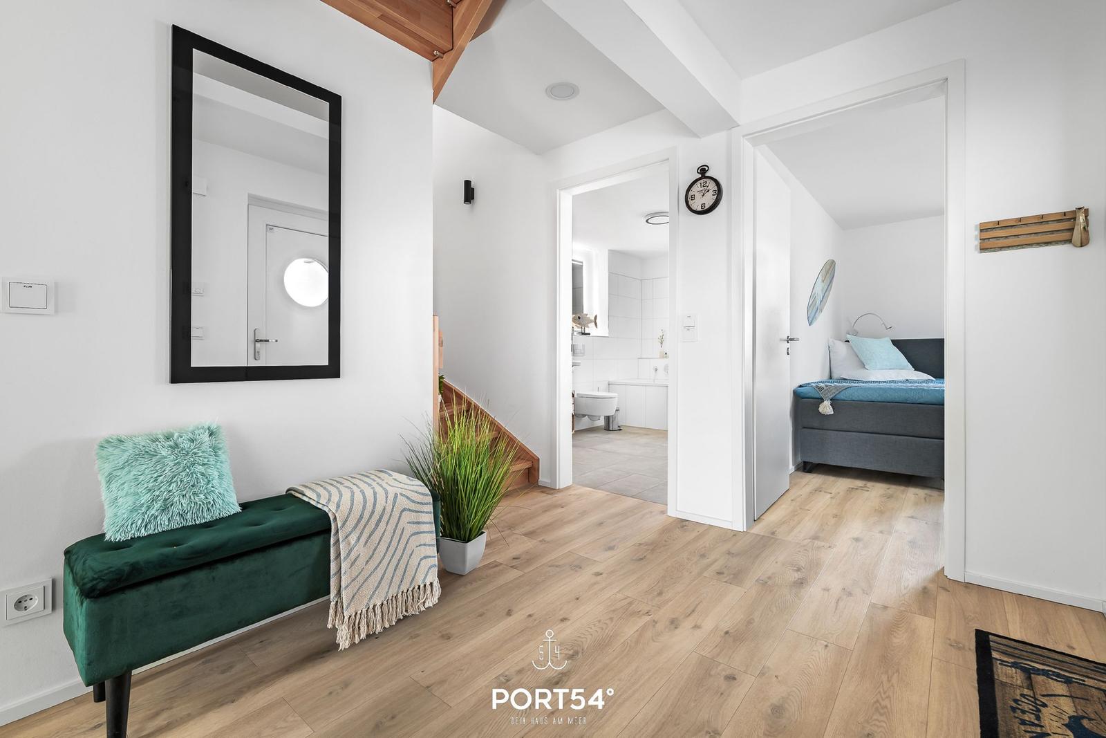 Eingangsbereich mit grünem Sitzbank, Spiegel und Blick in Schlafzimmer und Bad.
