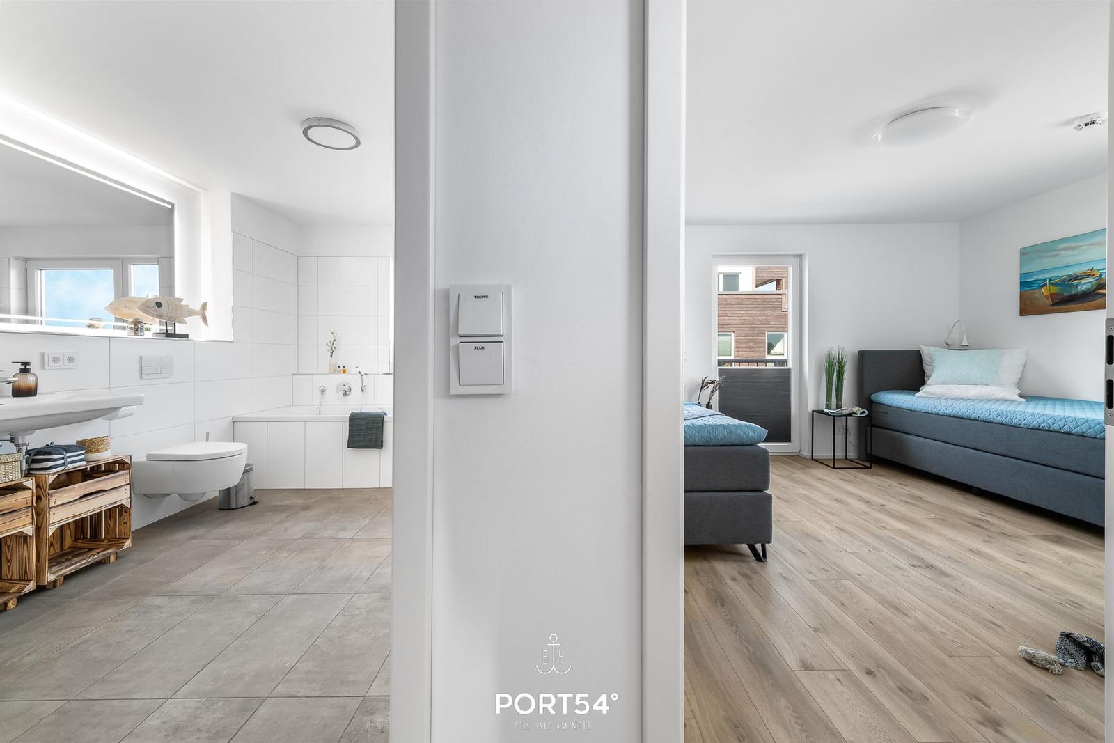 Badezimmer mit Badewanne und Toilette. Nebenraum mit Schlafsofa und Fenster.