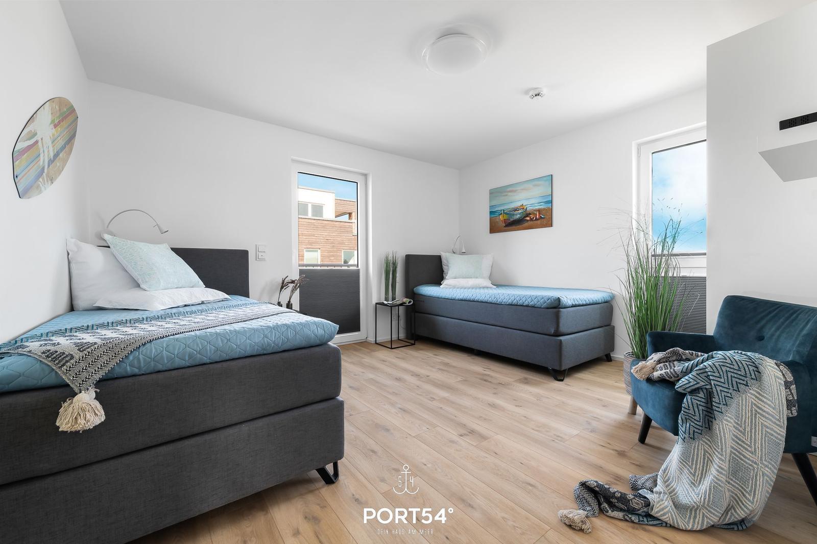Zimmer mit zwei Betten, blauen Decken und Holzboden. Fenster und Wandbild sichtbar.