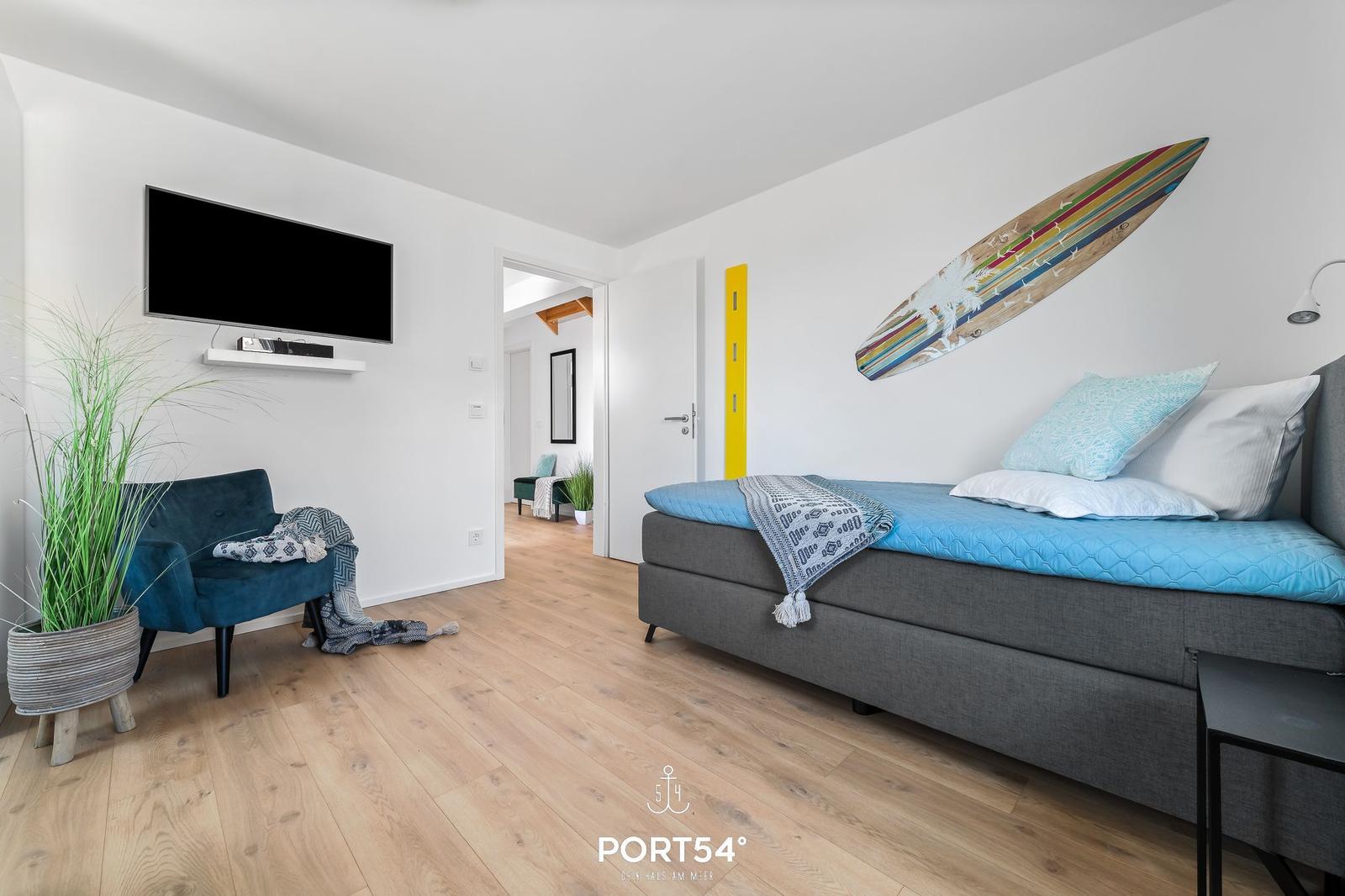 Schlafzimmer mit Bett, Fernseher und Pflanze. Wanddekoration mit Surfbrett.
