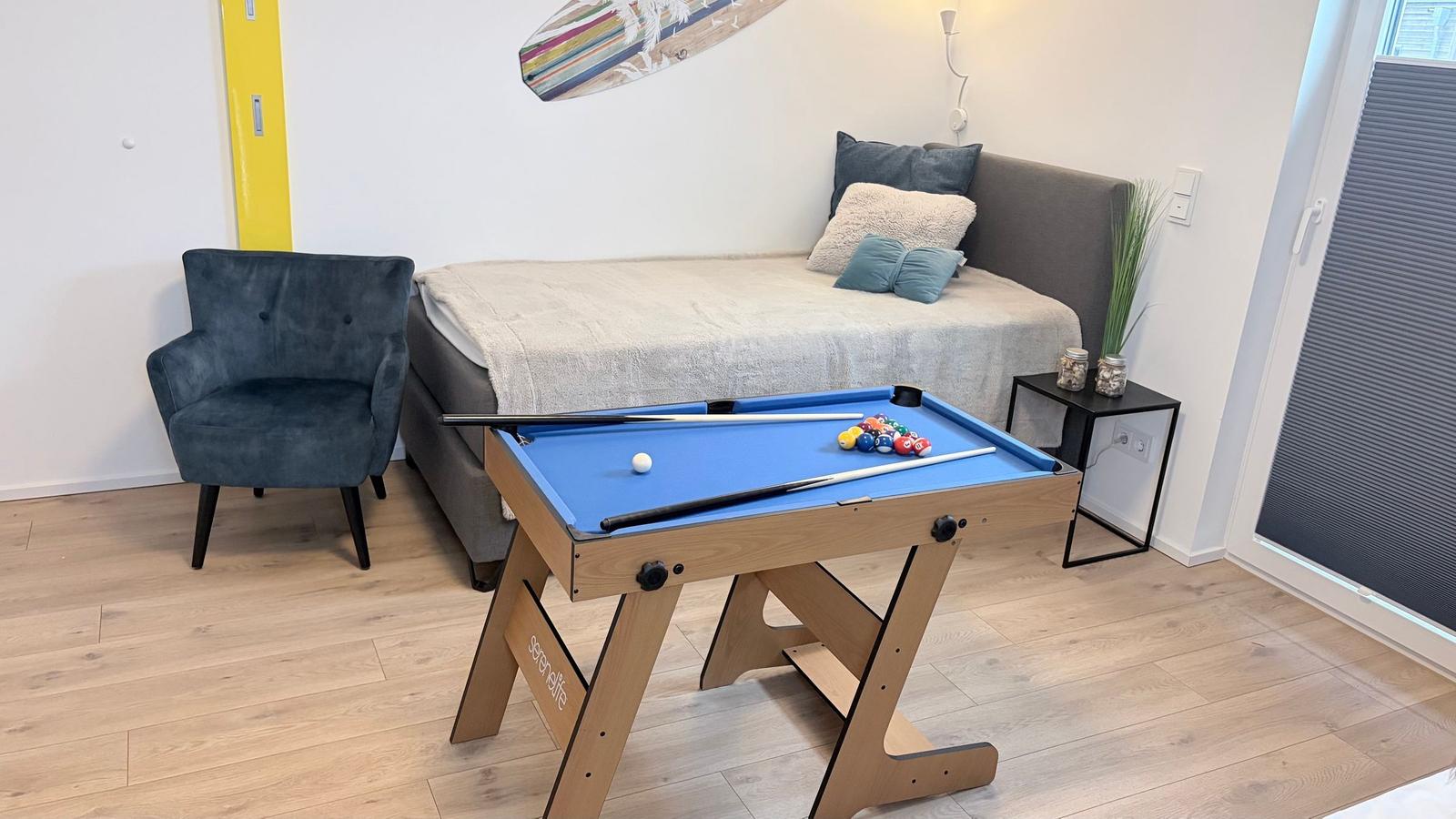 Ein Raum mit einem Billardtisch, einem Bett und einem Sessel.