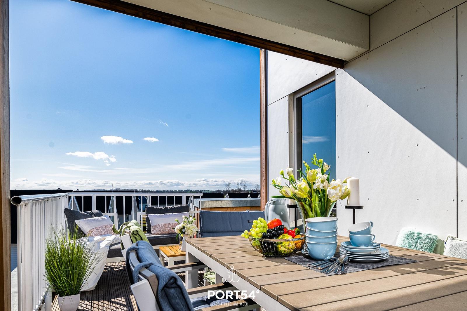 Terrasse mit Tisch, Stühlen und Blick auf den Himmel.
