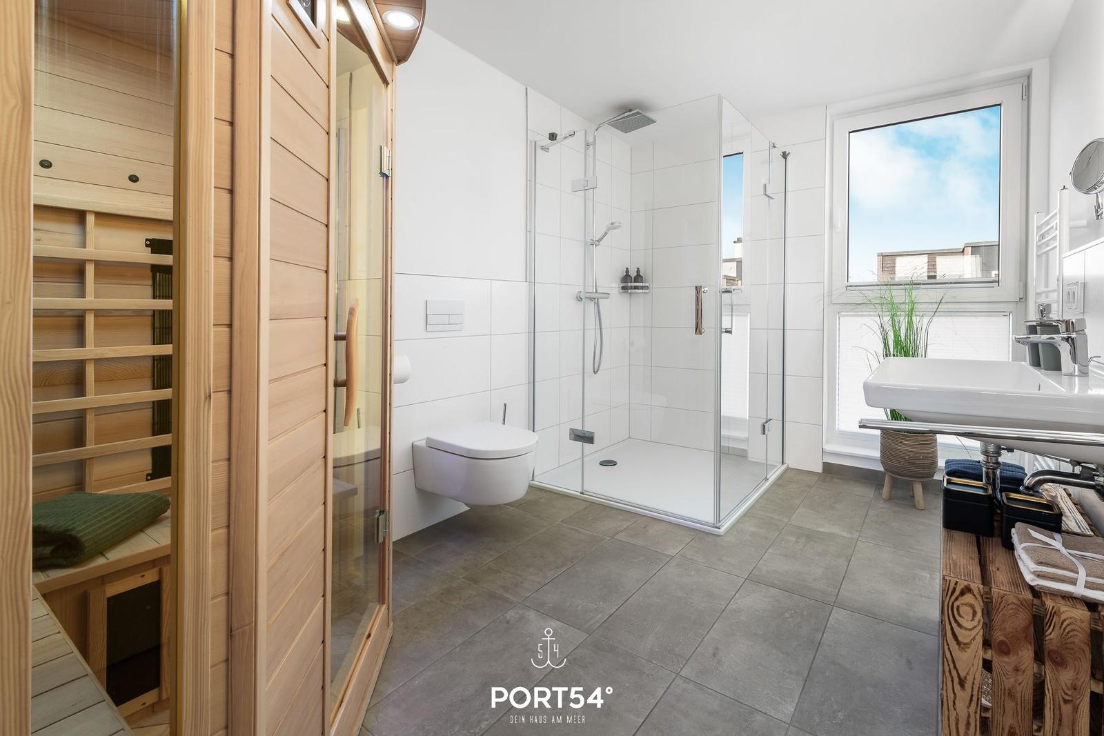 Badezimmer mit Dusche, Toilette und Sauna. Fenster mit Blick auf Außenbereich.