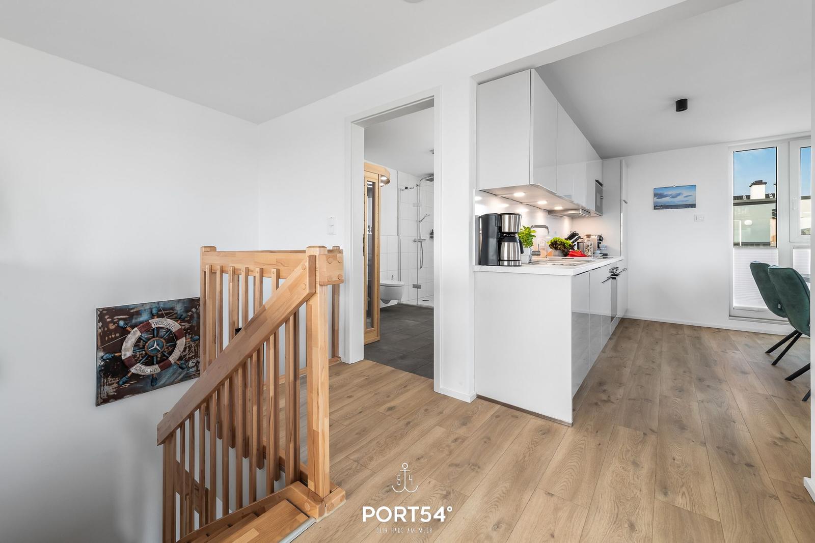 Küche mit Arbeitsplatz, Treppenhaus und Badezimmer im Hintergrund.
