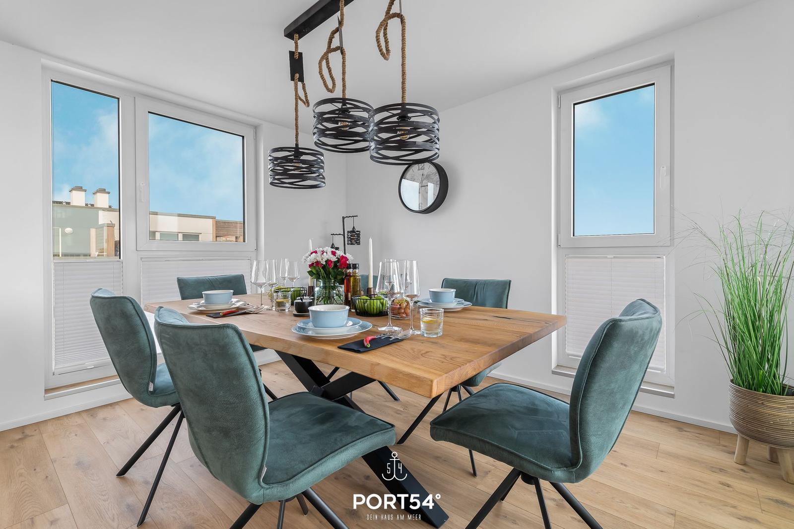 Esszimmer mit Holztisch, grünen Stühlen und moderner Hängelampe.