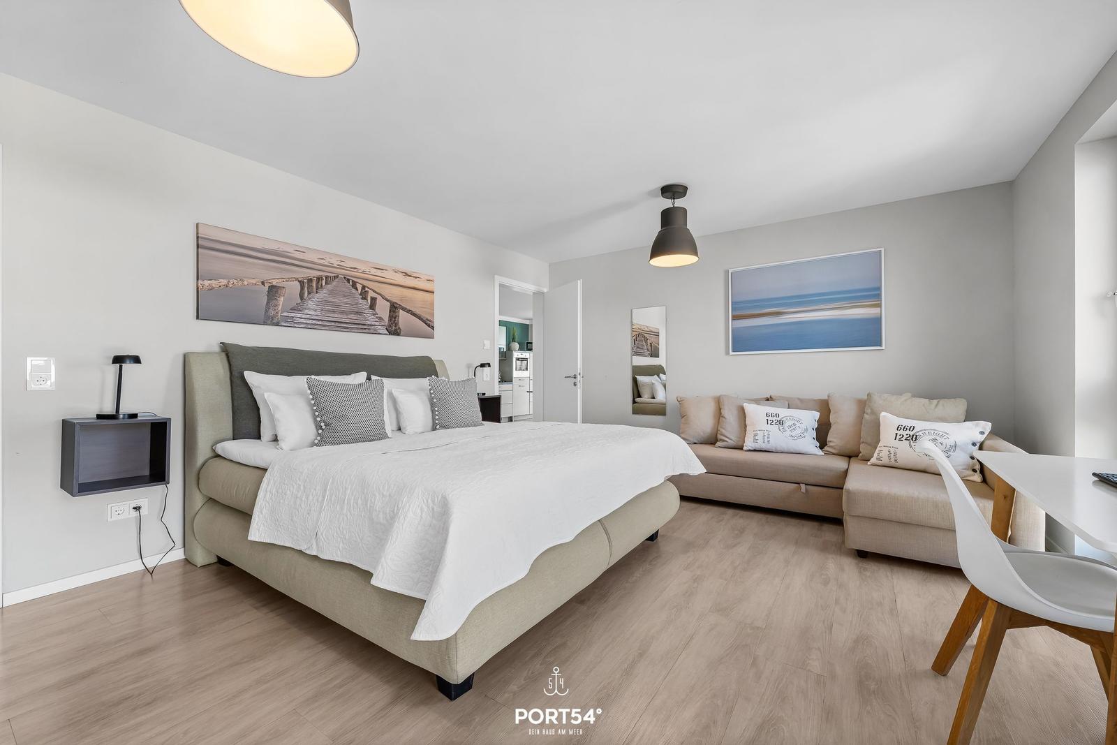 Schlafzimmer mit Bett, Sofa und Wandbildern. Holzboden und moderne Beleuchtung.
