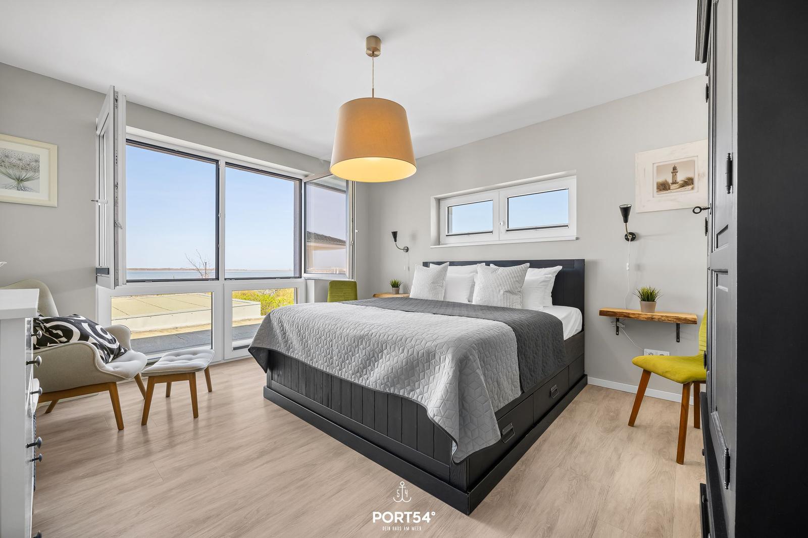 Schlafzimmer mit Blick auf Wasser, Bett, Sessel und Fenster.