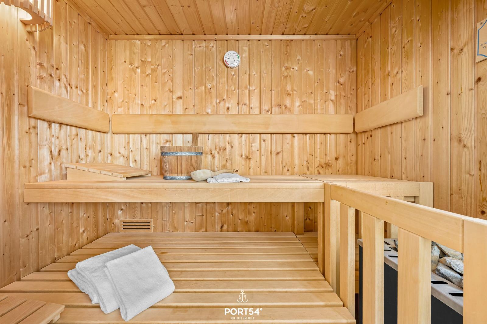 Sauna mit Holzbänken, Thermometer und Handtuch.