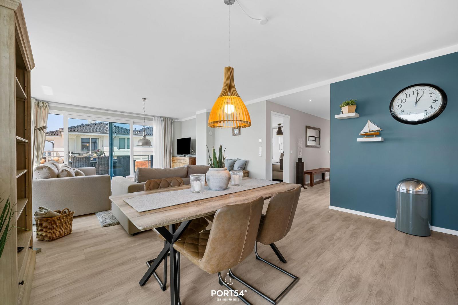 Essbereich mit Holztisch und Stühlen. Hintergrund: Wohnbereich mit Sofa und Terrasse.
