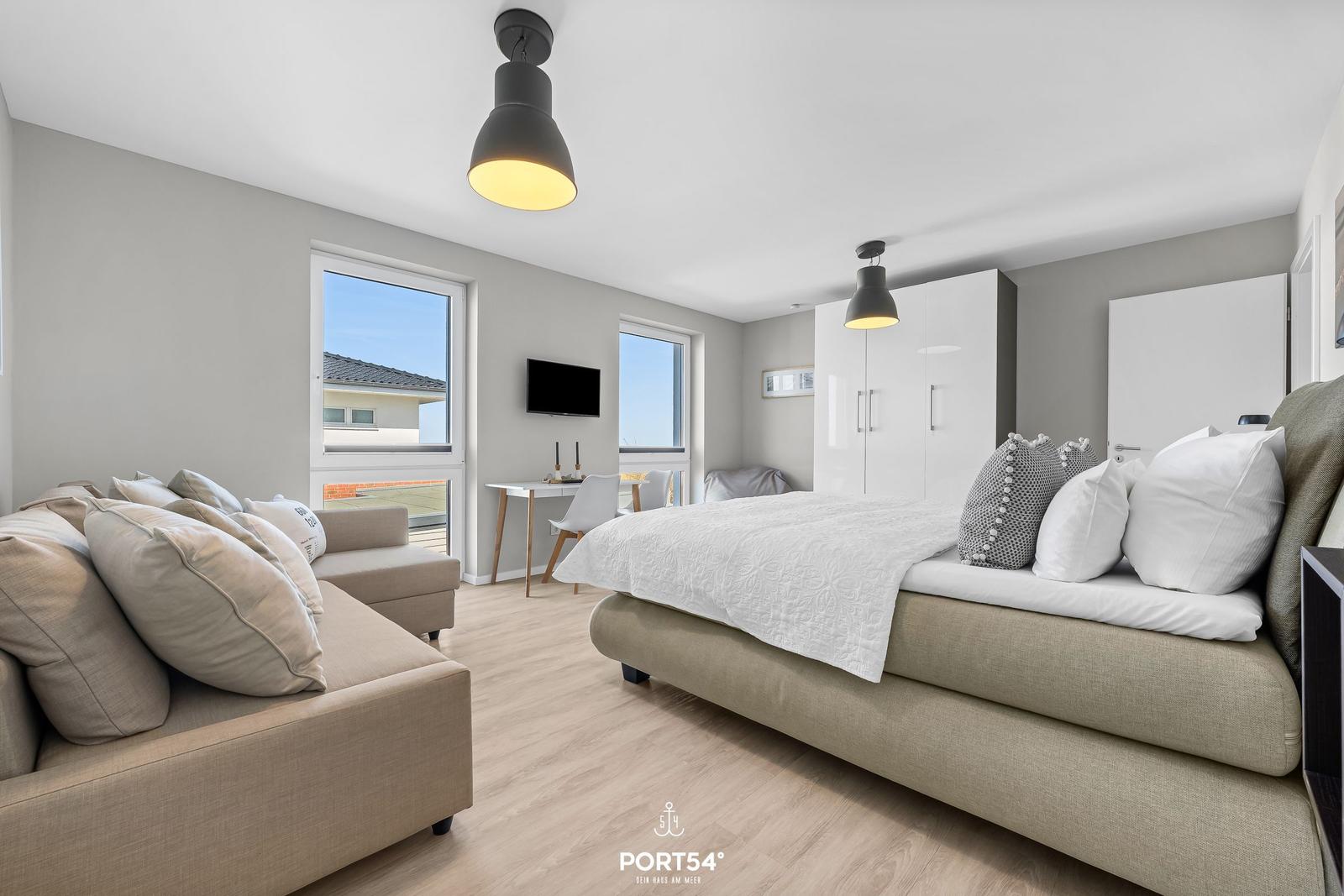 Schlafzimmer mit Bett, Sofa und Fenstern zum Balkon.