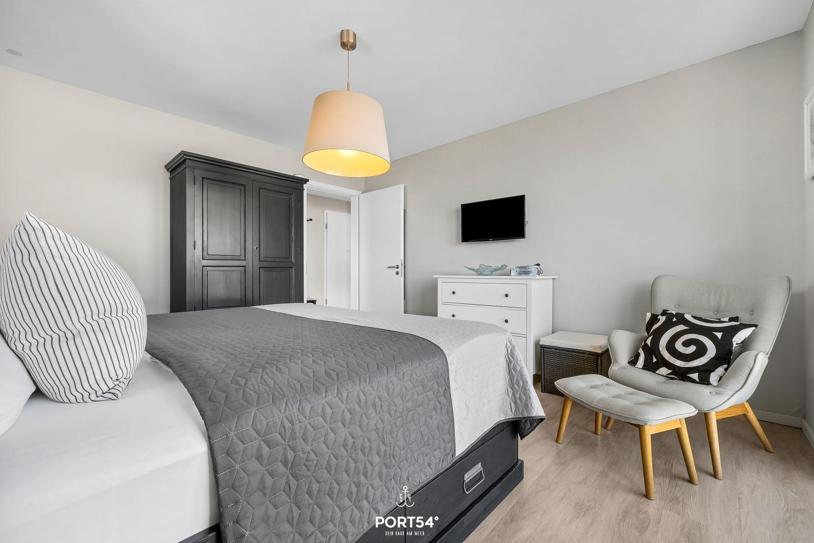 Schlafzimmer mit Bett, Kleiderschrank, TV und Sessel.