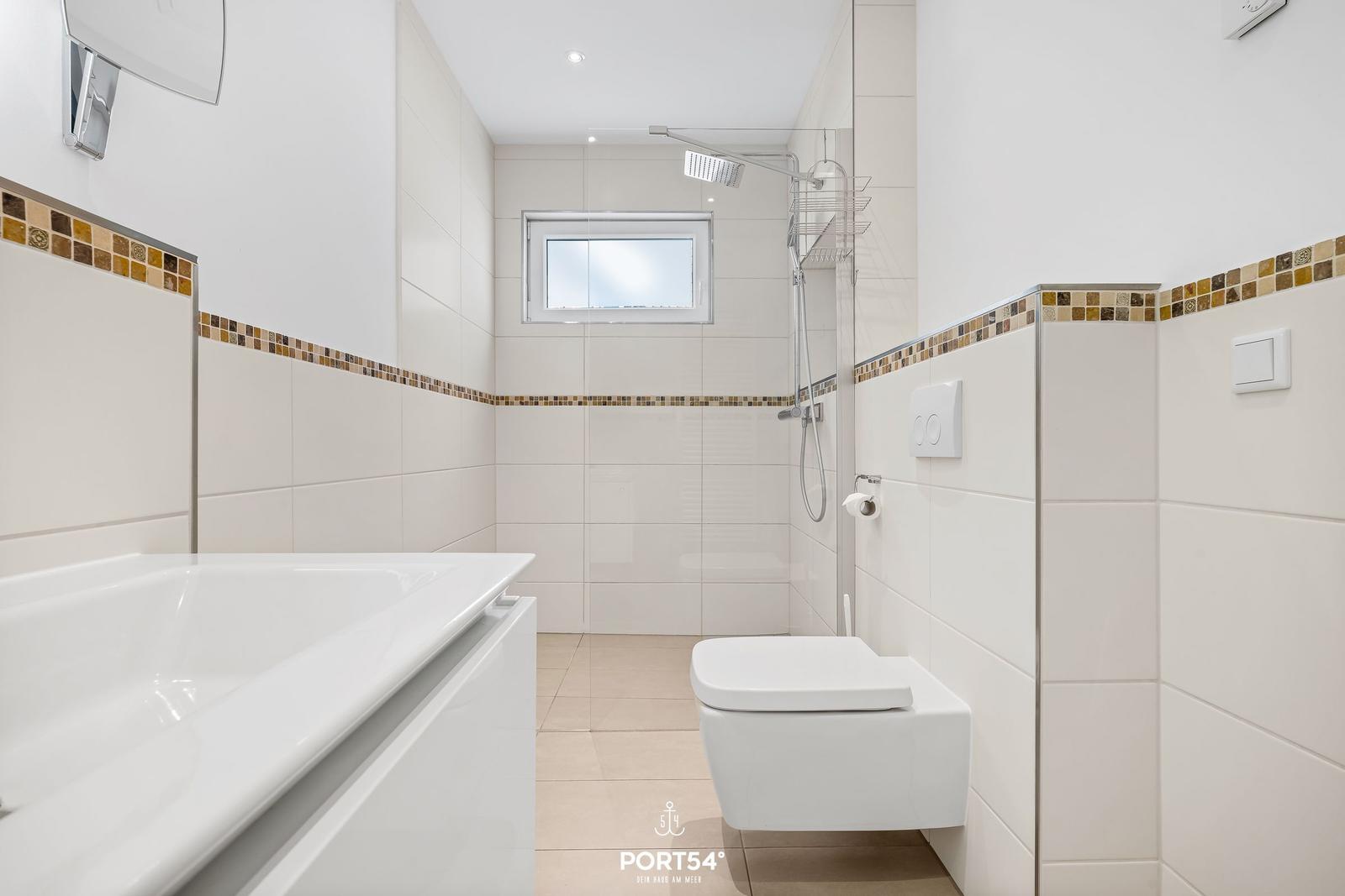 Badezimmer mit Dusche, Badewanne und Toilette. Wandfliesen mit Mosaikstreifen.