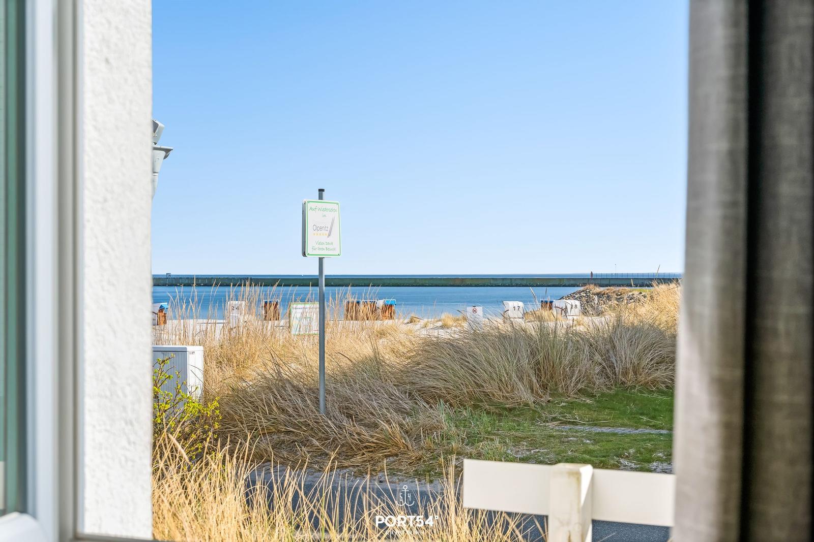 Blick vom Fenster auf Strand und Watt mit Schild und Strandkörben.