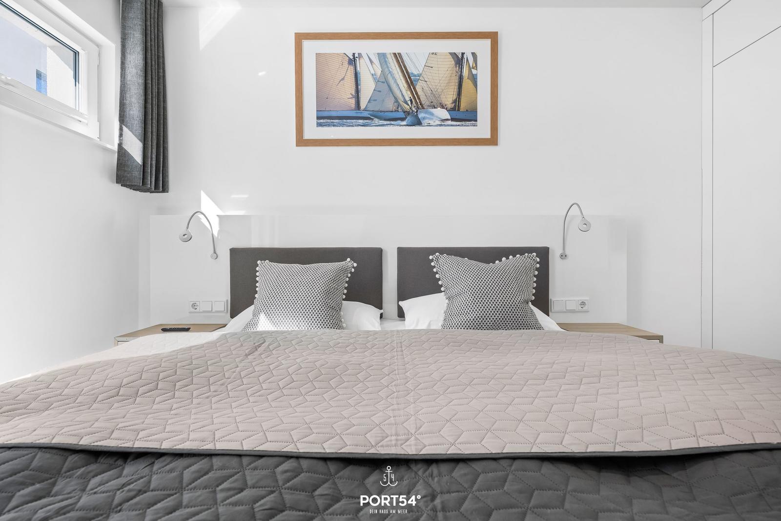 Schlafzimmer mit Doppelbett, Wandbild und Nachttischen mit Lampen.