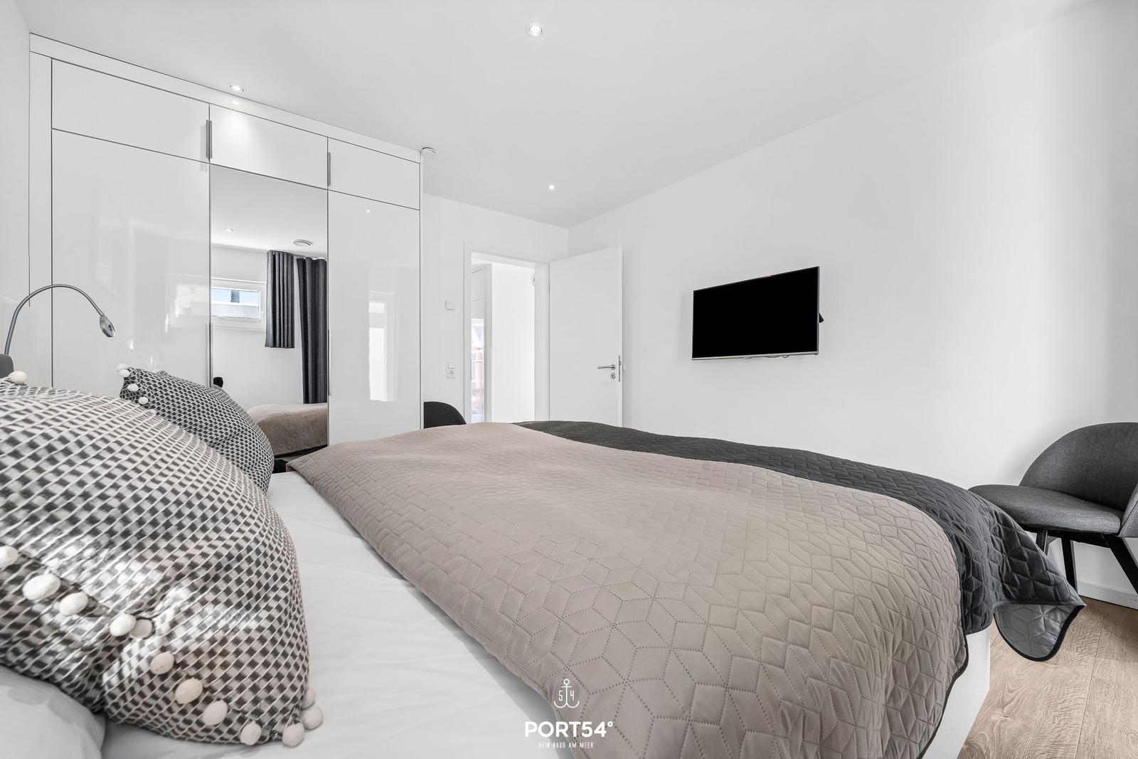 Schlafzimmer mit Bett, Kleiderschrank und Wandfernseher.