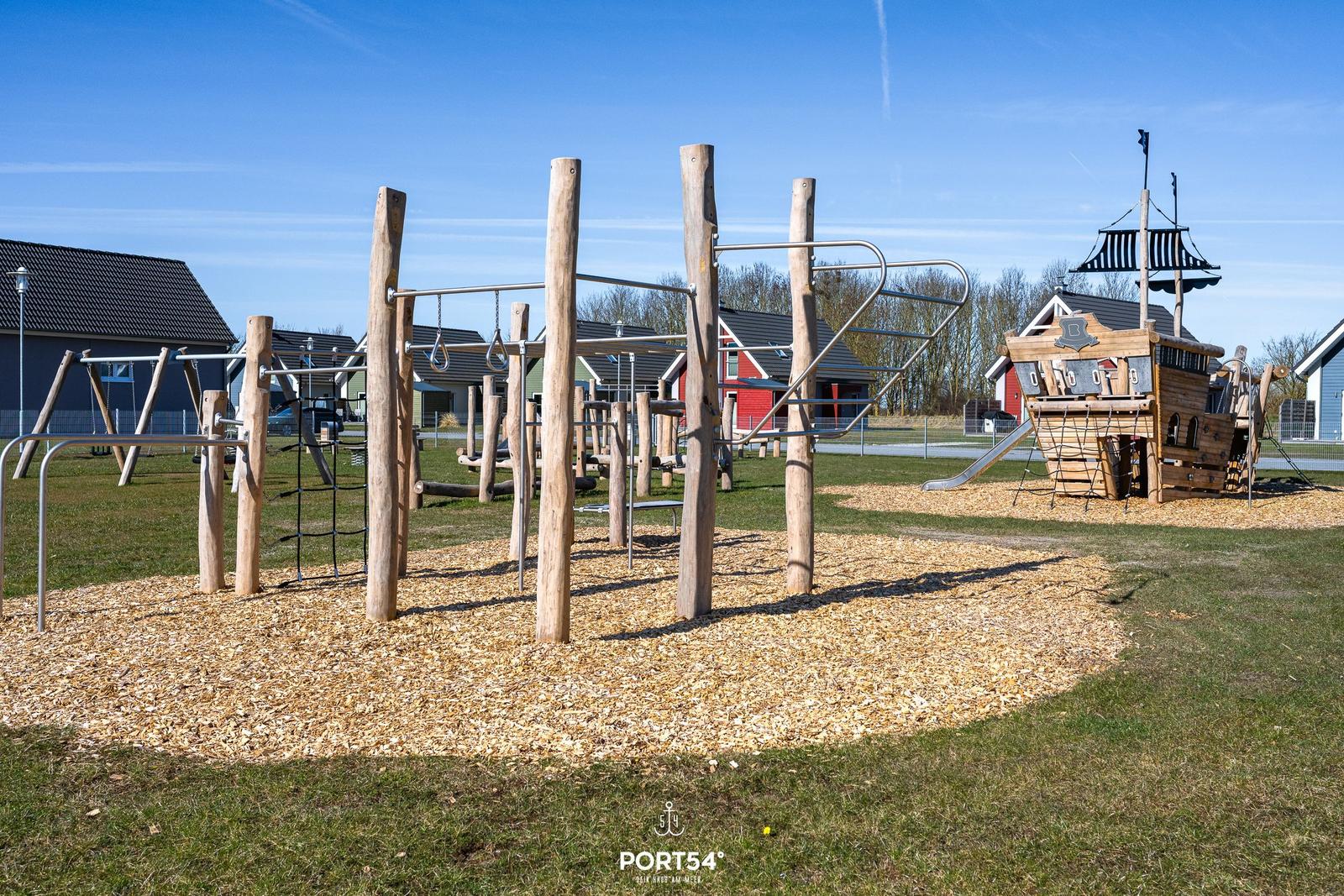 Kinder-Spielplatz mit Holz- und Metallgeräten auf Kies und Gras.