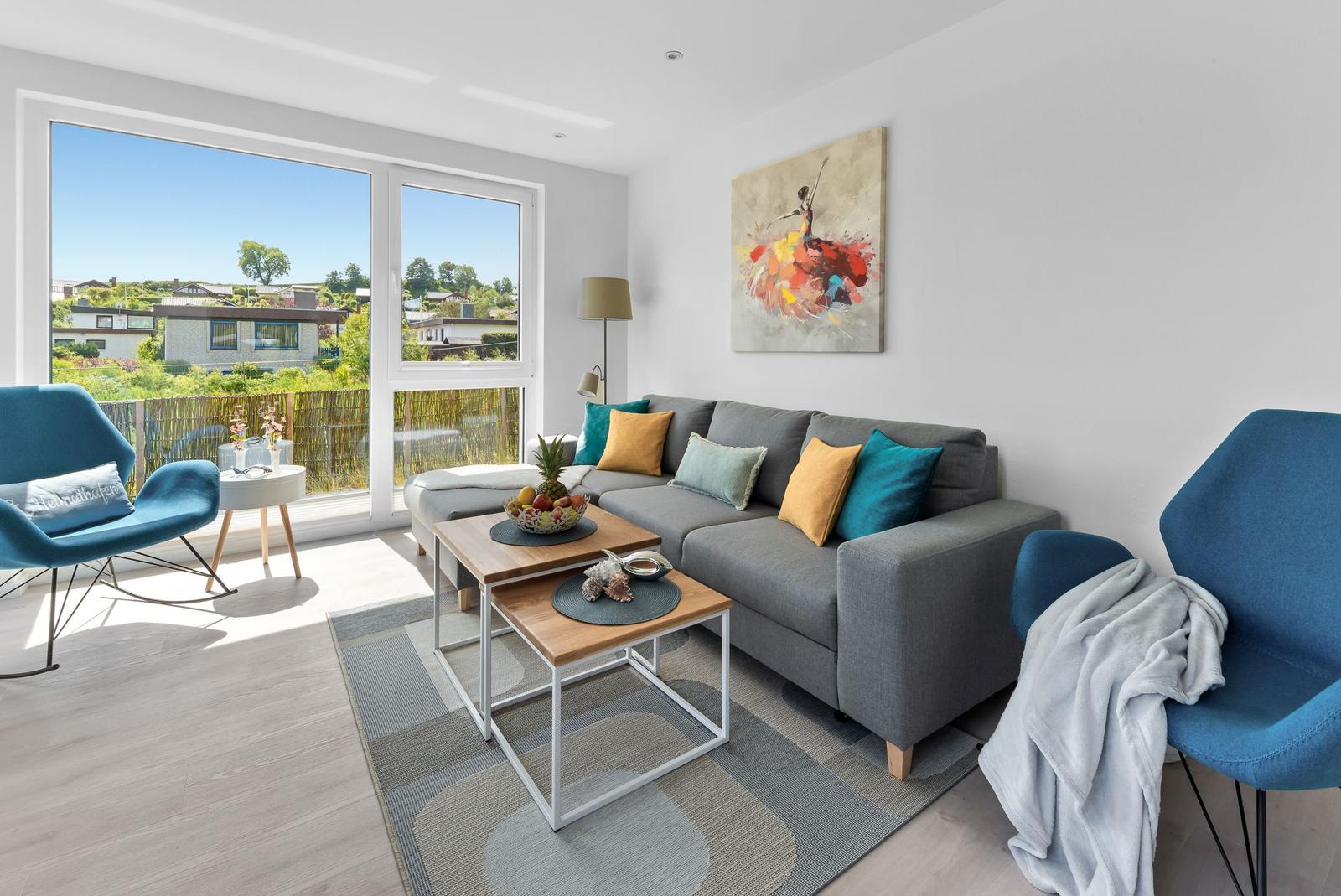 A living room with a gray sofa, blue chairs, and large windows overlooking the terrace.