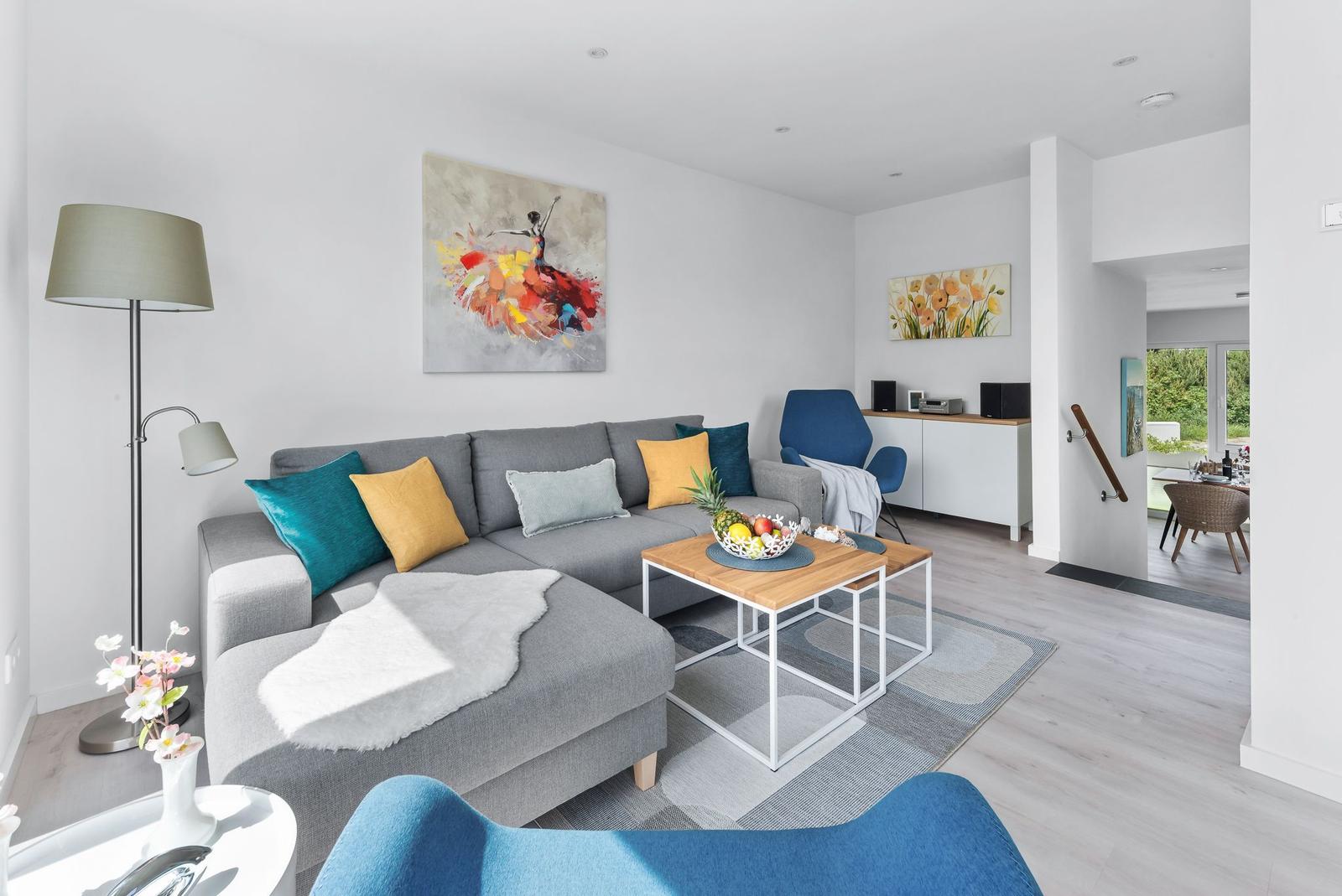Living room with gray sofa, blue and yellow cushions, wooden table, and wall art.