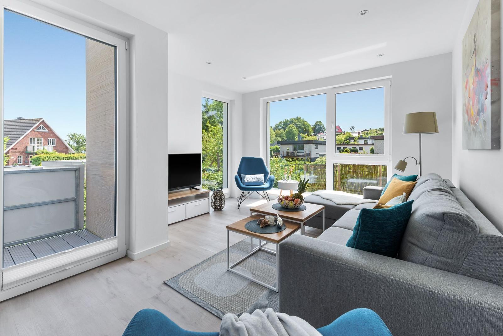 Living room with large sofa, TV, and view of balcony and garden.
