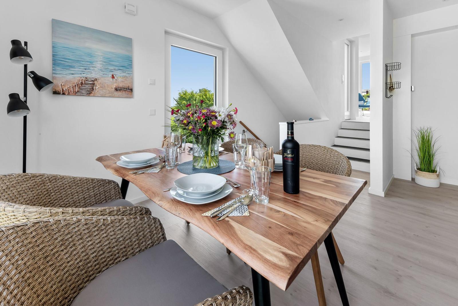 Dining table with chairs, flowers, and wine bottle by window with view.