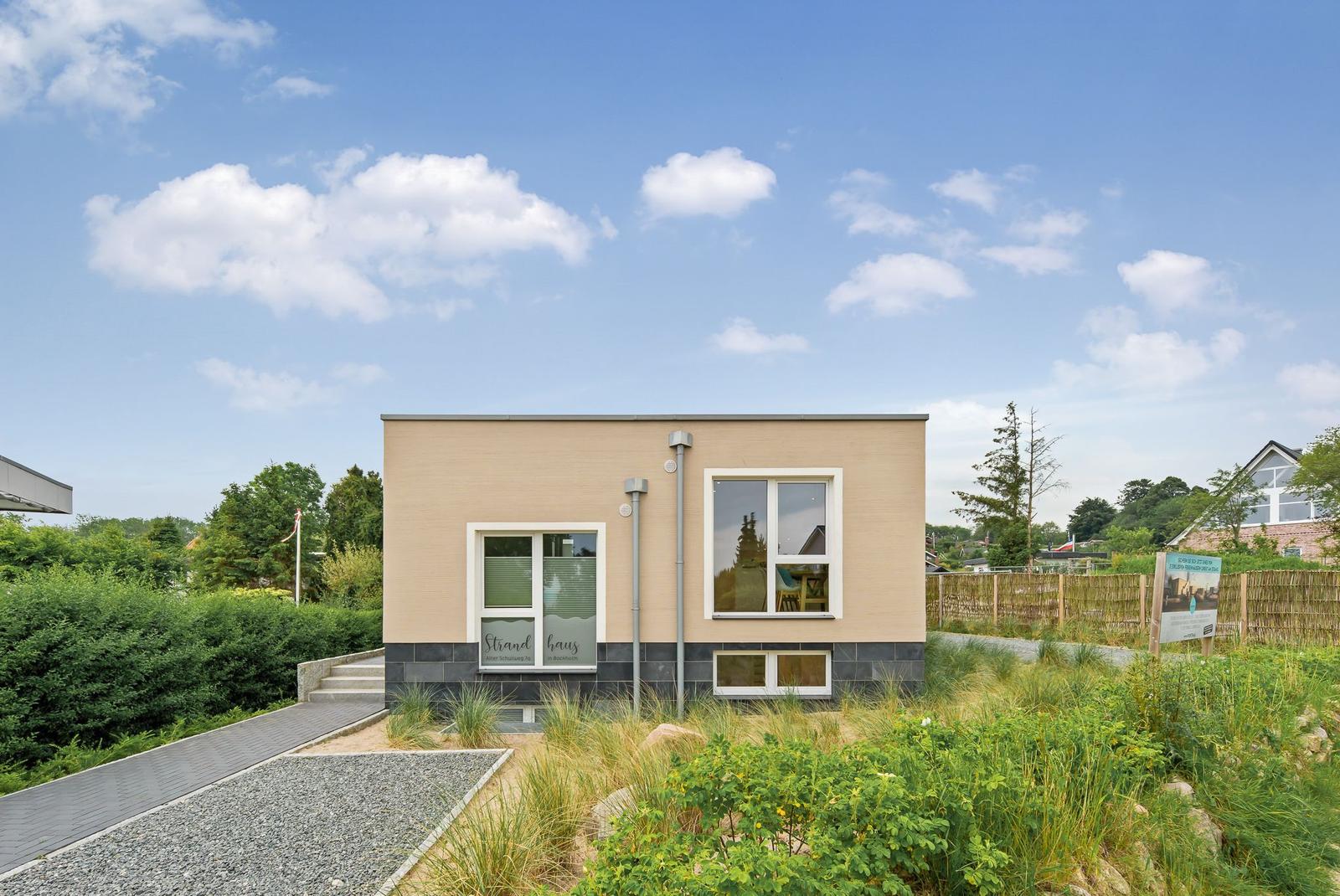 Modern vacation home with large windows and landscaped garden under blue sky.