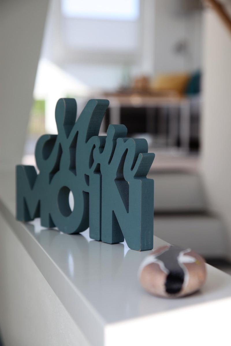 Wooden sign with Moin Moin on a white surface. A living area is visible in the background.