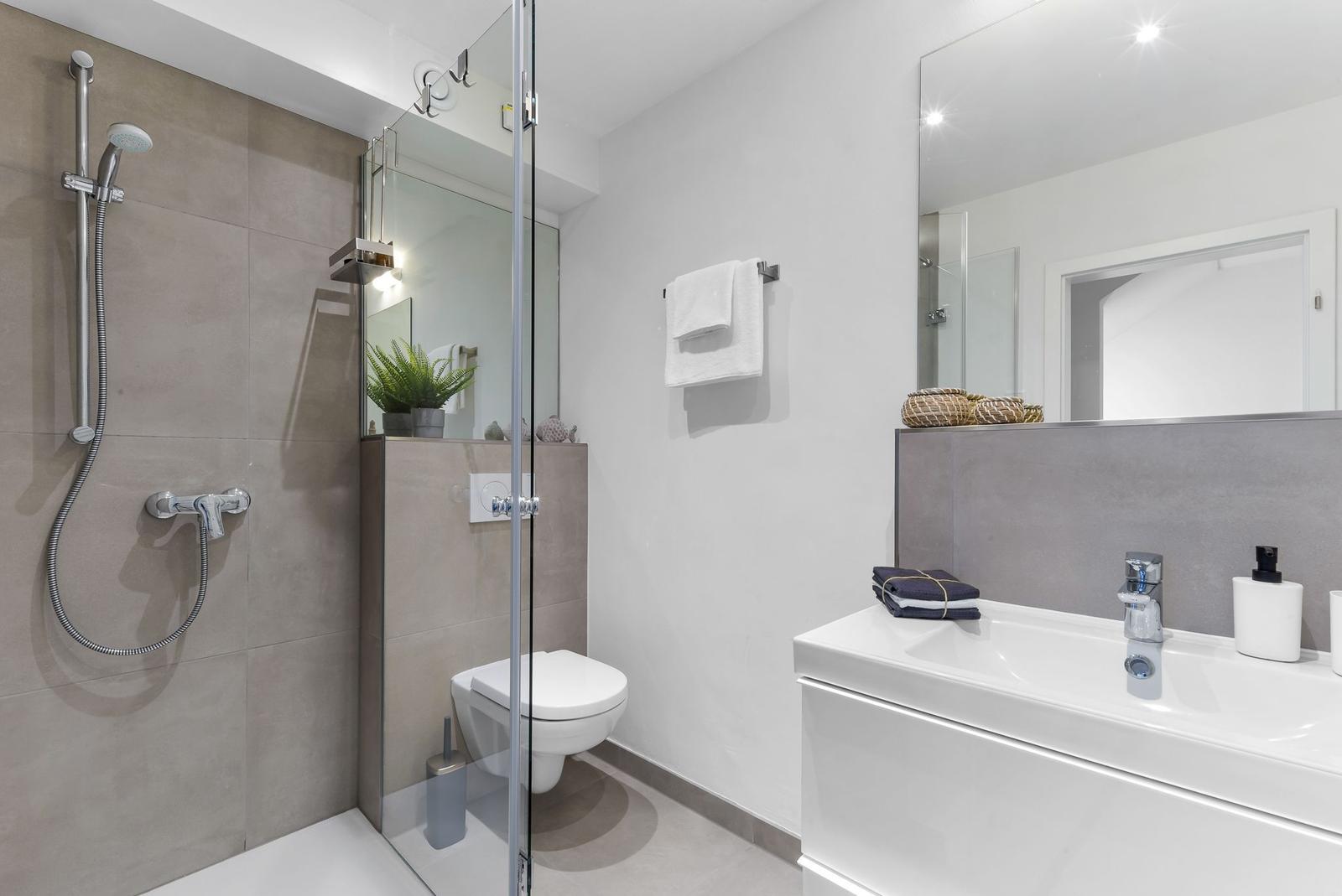 Bathroom with shower, toilet, and sink. Light wall color and modern furnishings.