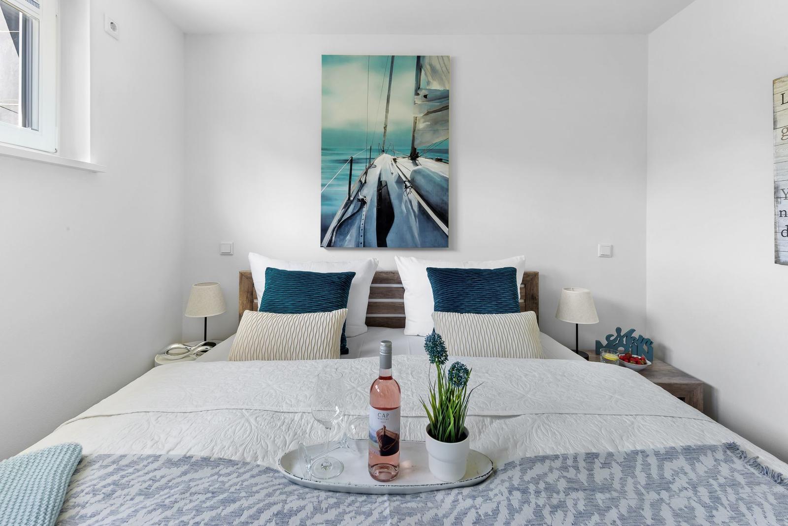 Bedroom with bed, wall art, and nightstands. On the bed is a tray with wine and plant.