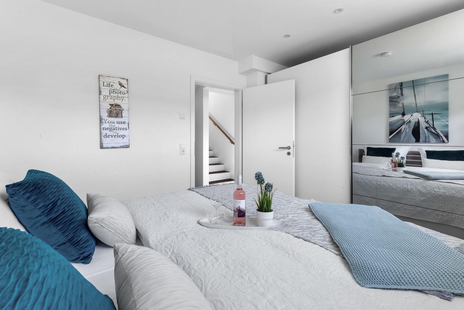 Bedroom with bed, wall mirror, and staircase. On bed is a bottle and plant.