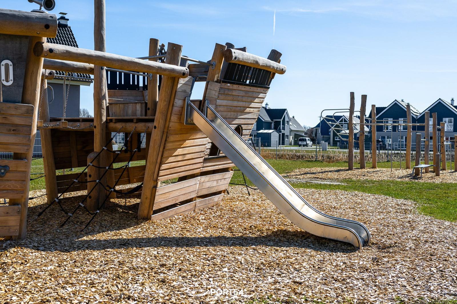 Holzspielplatz mit Rutsche und Klettergerüst auf Kiesfläche