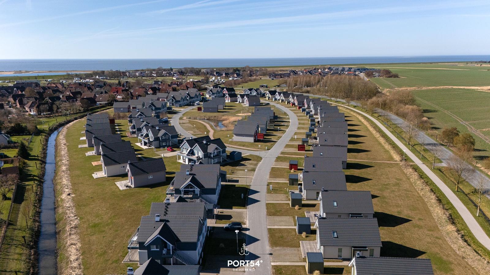 Aerielansicht eines Ferienorts mit Häusern, Straßen und Meer im Hintergrund.