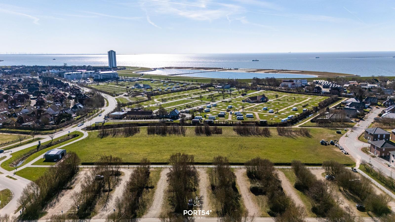 Aerial view of a coastal campsite with green fields, parked caravans, and a sea view.