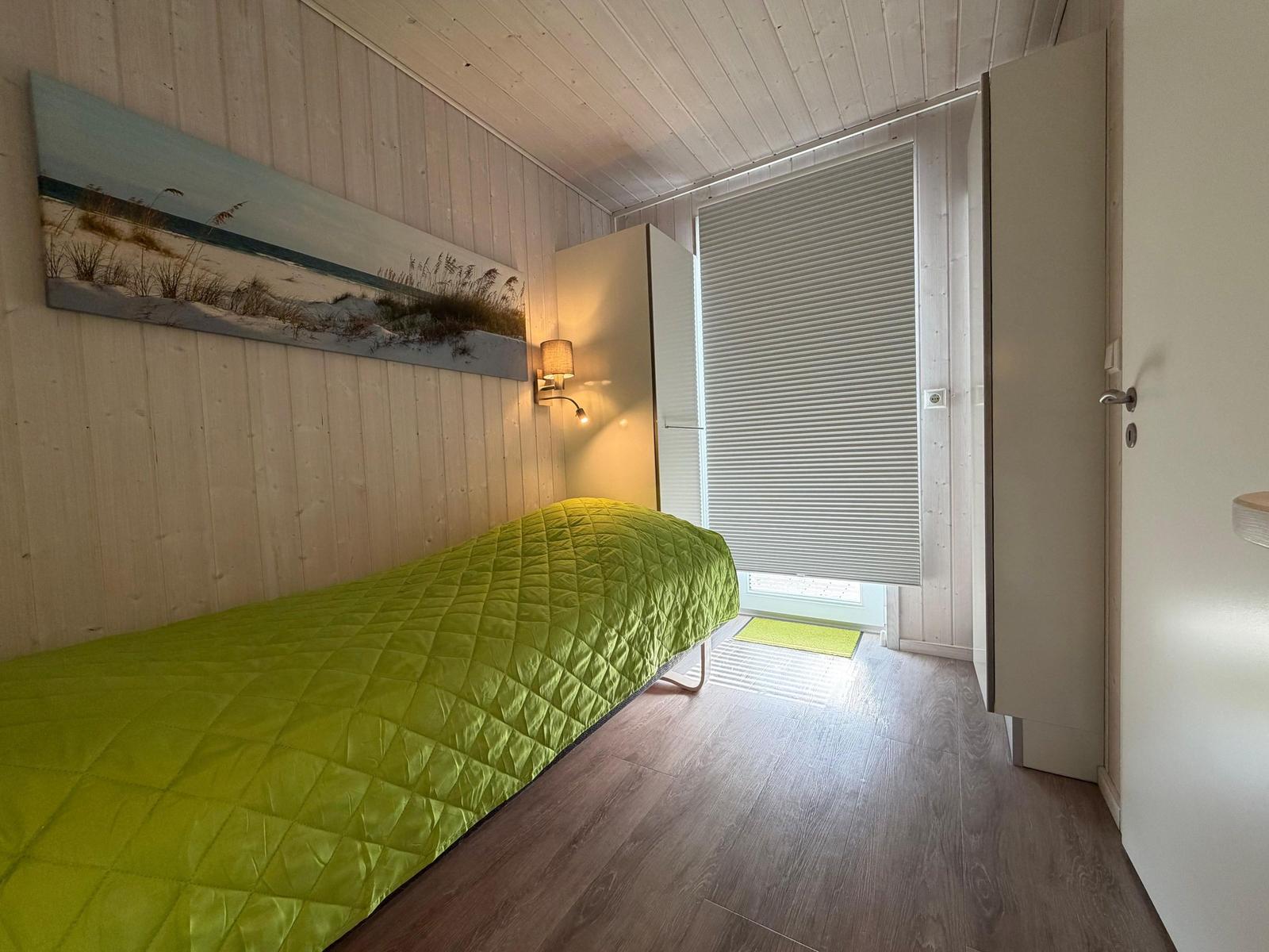 Bedroom with bed, wall art, and wood floor. Door leads outside.
