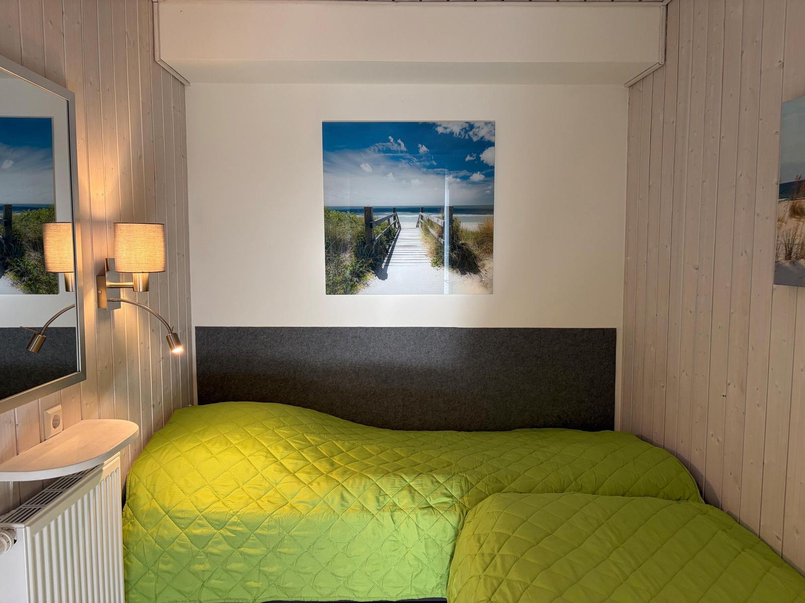 Bedroom with bed, wall art, and lamps on wood wall.