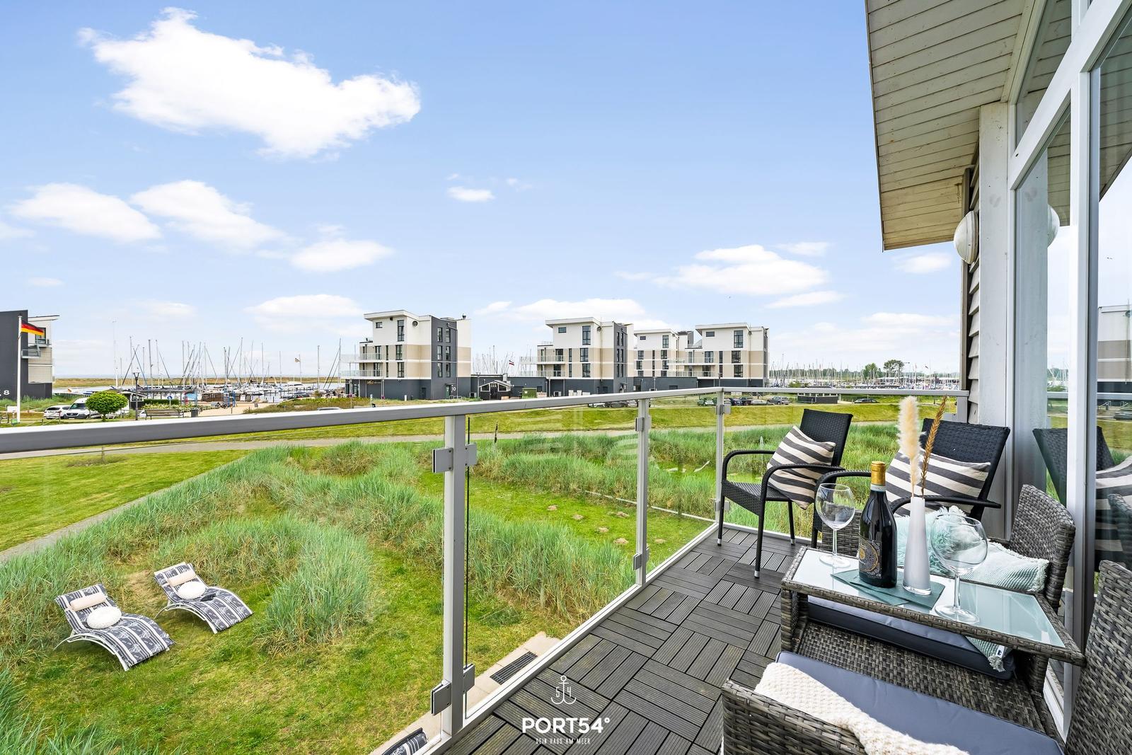 Terrasse mit Sitzgelegenheiten und Blick auf den Hafen und Grünflächen.
