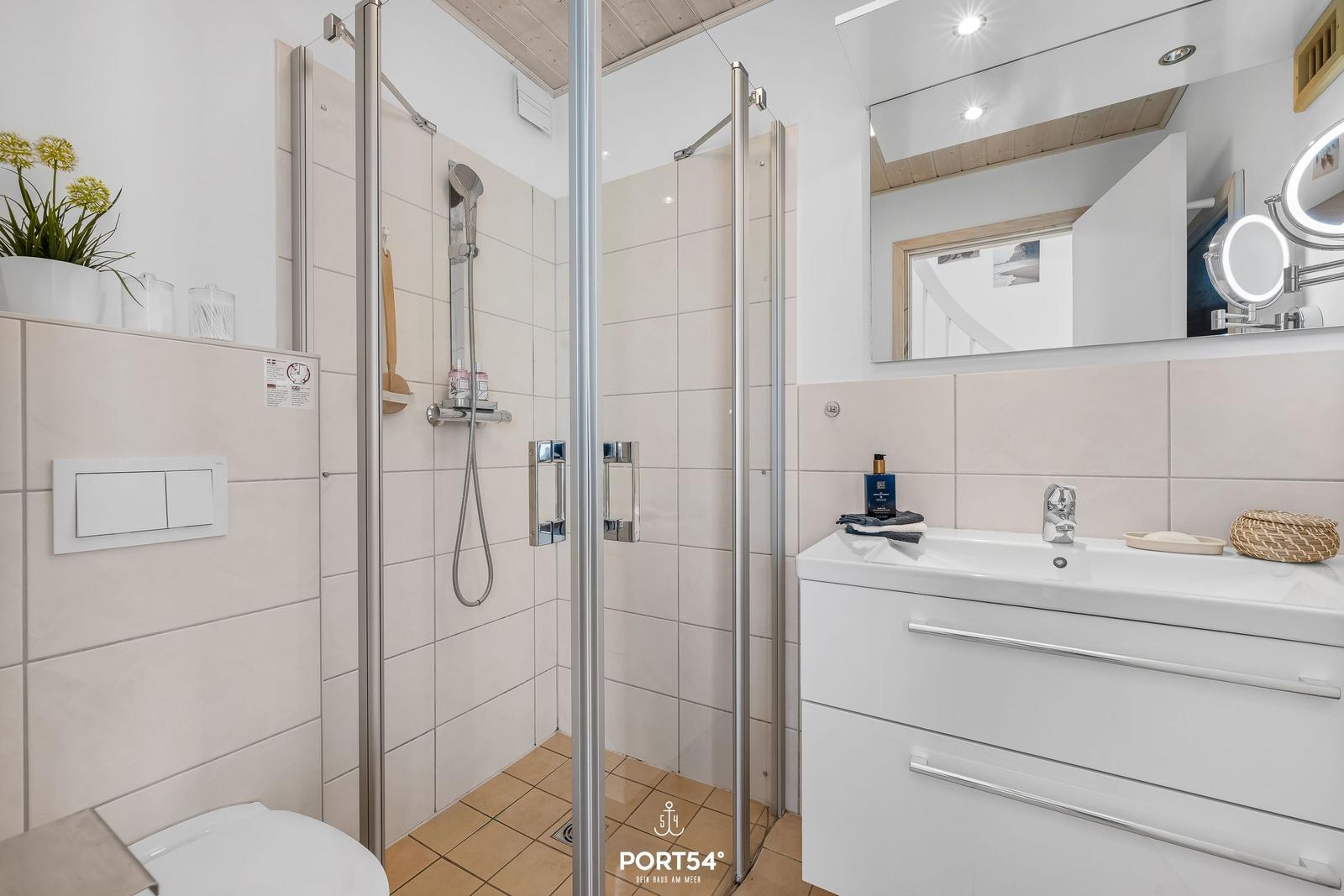Badezimmer mit Dusche, Waschbecken und Spiegel. Fliesenwand und weißer Waschtisch.