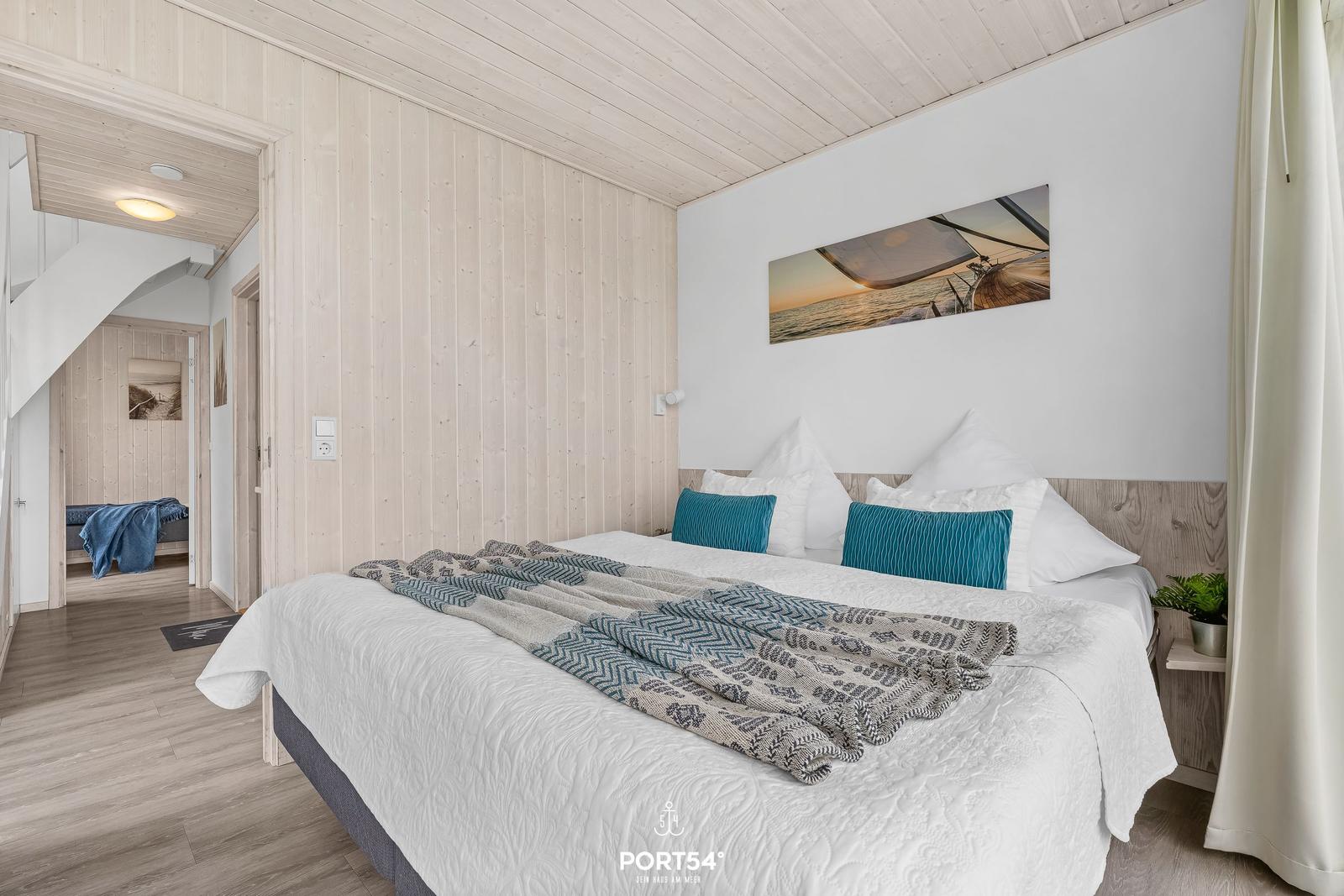Schlafzimmer mit Doppelbett, Holzwand und Wandbild. Blick in angrenzenden Raum.
