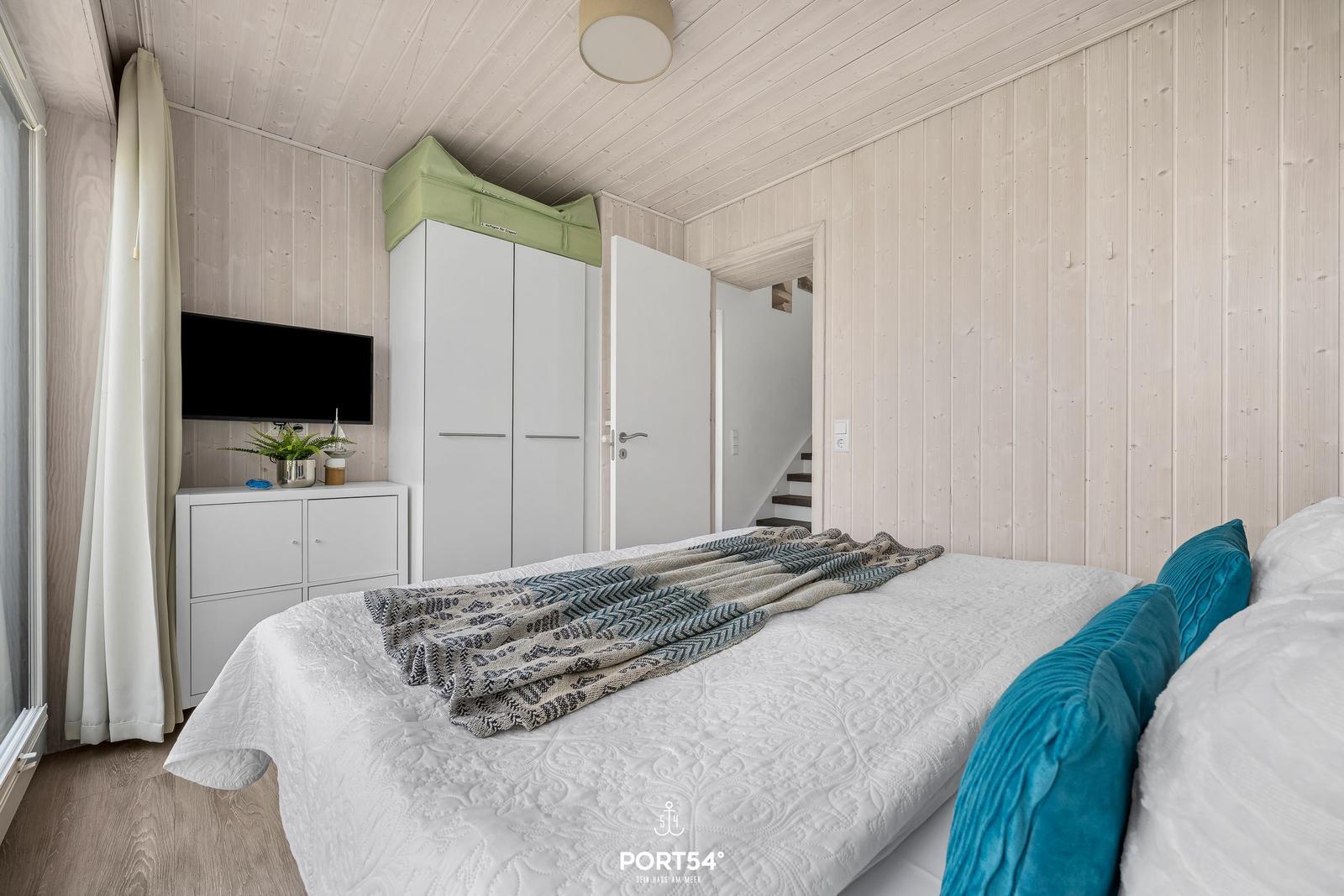 Schlafzimmer mit Bett, Kleiderschrank und Fernseher an der Wand.