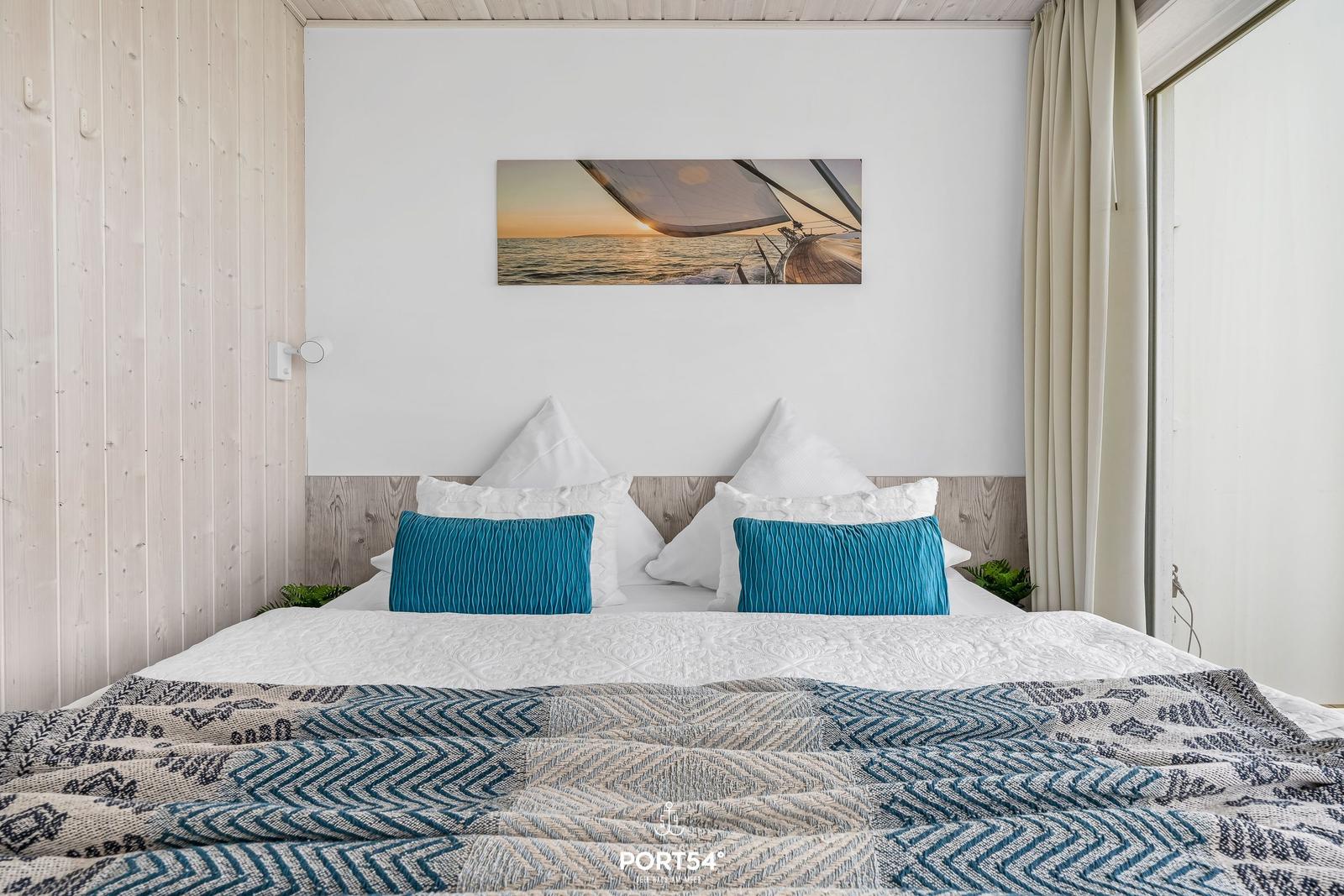 Doppelbett mit blauen Kissen und Musterdecke unter Wandbild mit Segelboot.