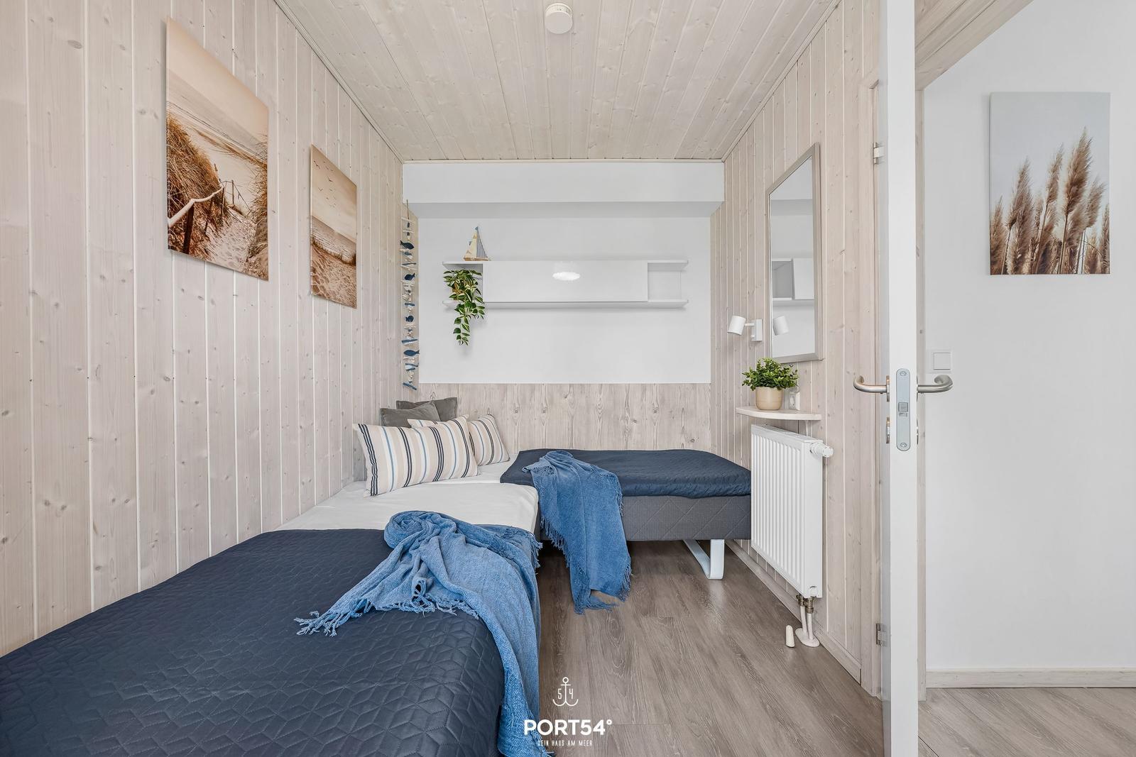 Zwei Betten mit blauen Decken, Holzwände und Wandbilder in einem Schlafzimmer.