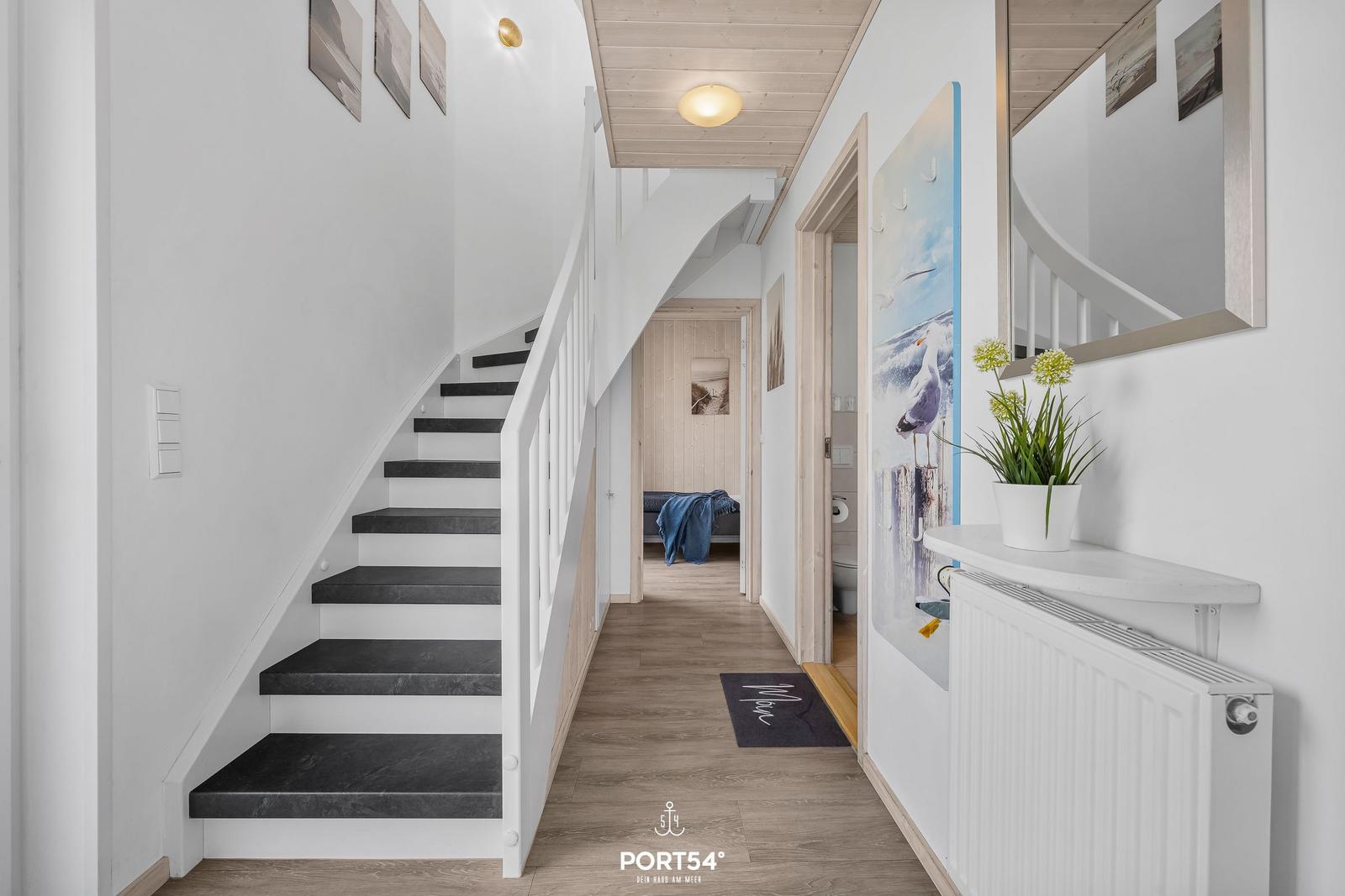 Hausflur mit Treppe, Wandbild und Pflanze. Blick in Schlafzimmer und Bad.