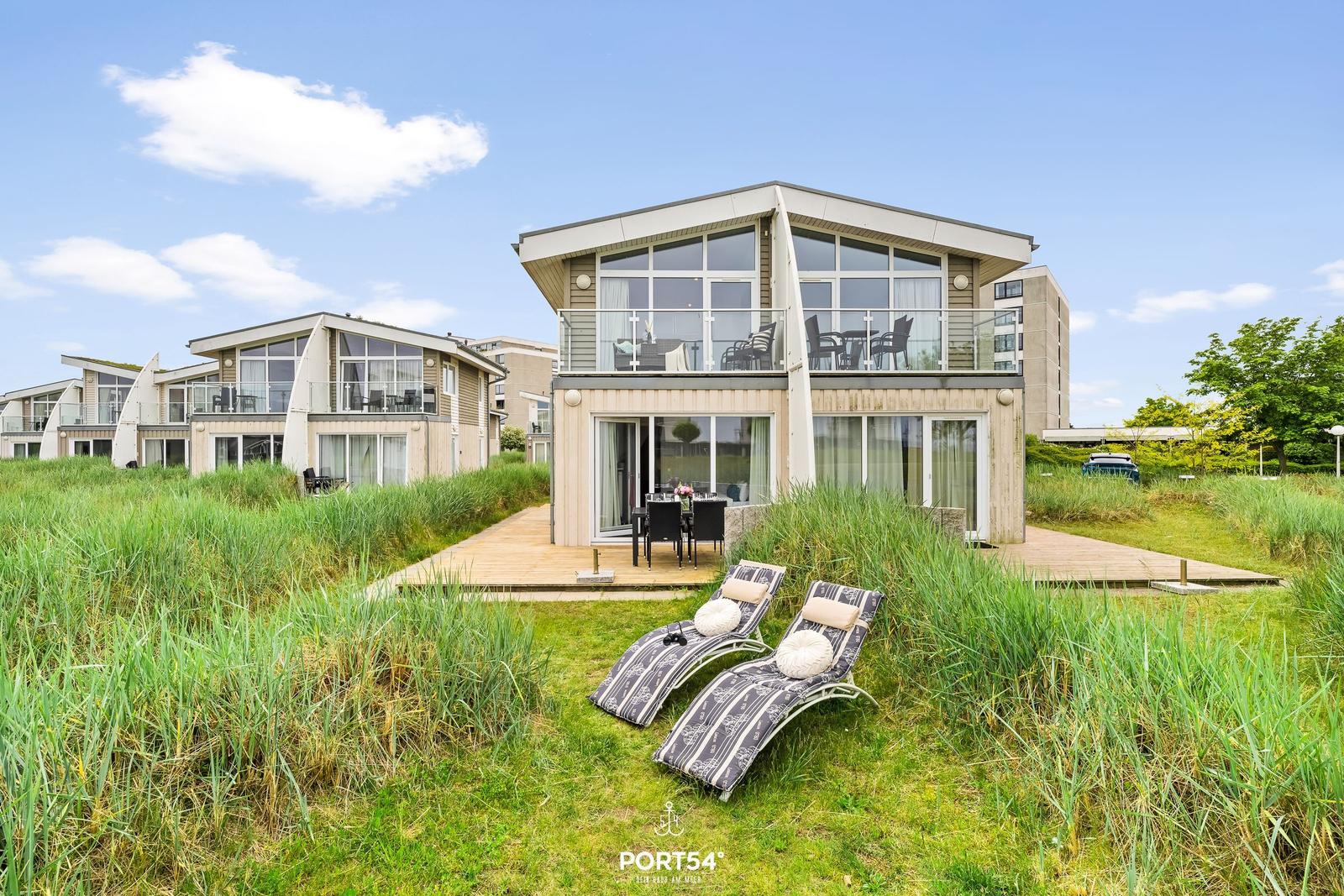 Moderne Villa mit Terrasse und Liegestühlen in Grasland