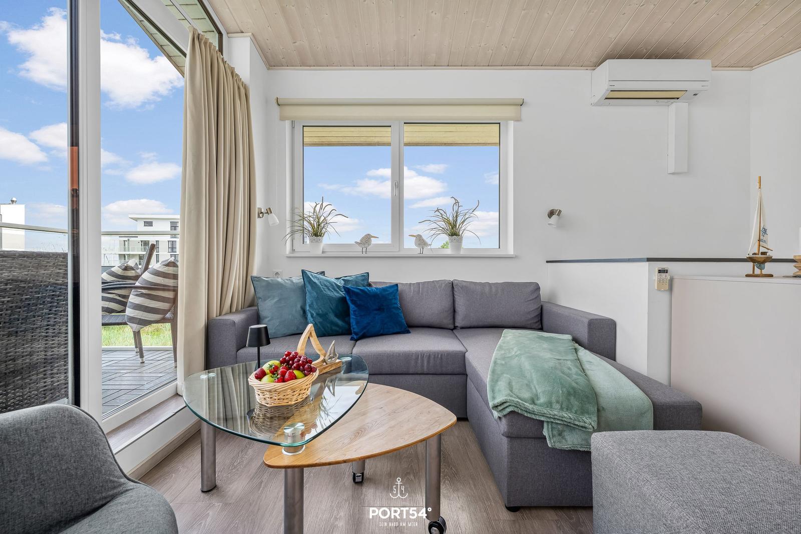 Ein Wohnbereich mit grauem Sofa, Glas-Tisch und Balkonansicht.
