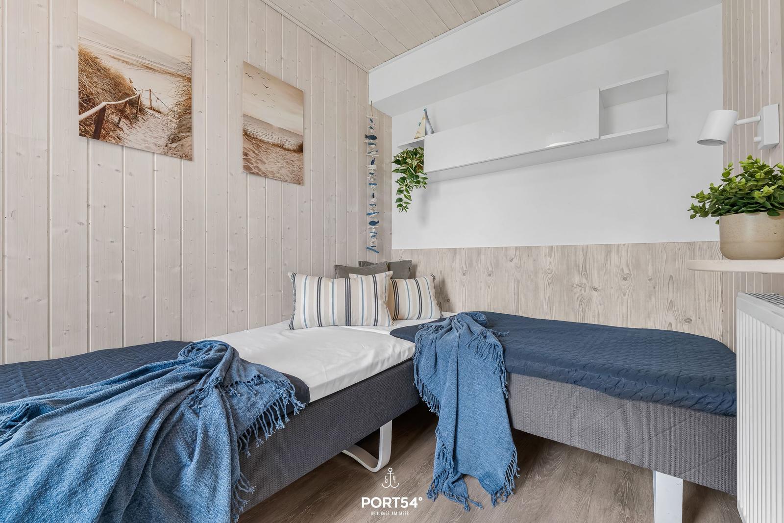 Zwei Betten mit blauen Decken und Kissen in einem Raum mit Holzwänden und Wandbildern.