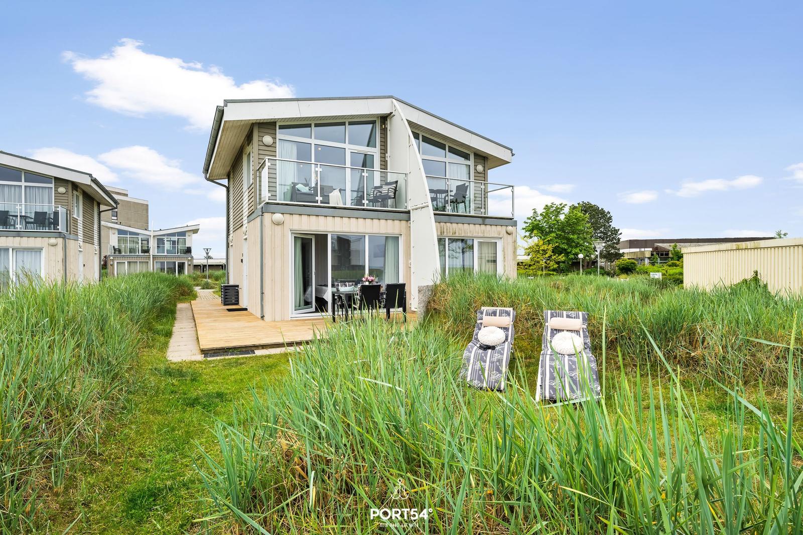 Moderne Ferienwohnung mit Balkon und Liegestühlen im Gras.