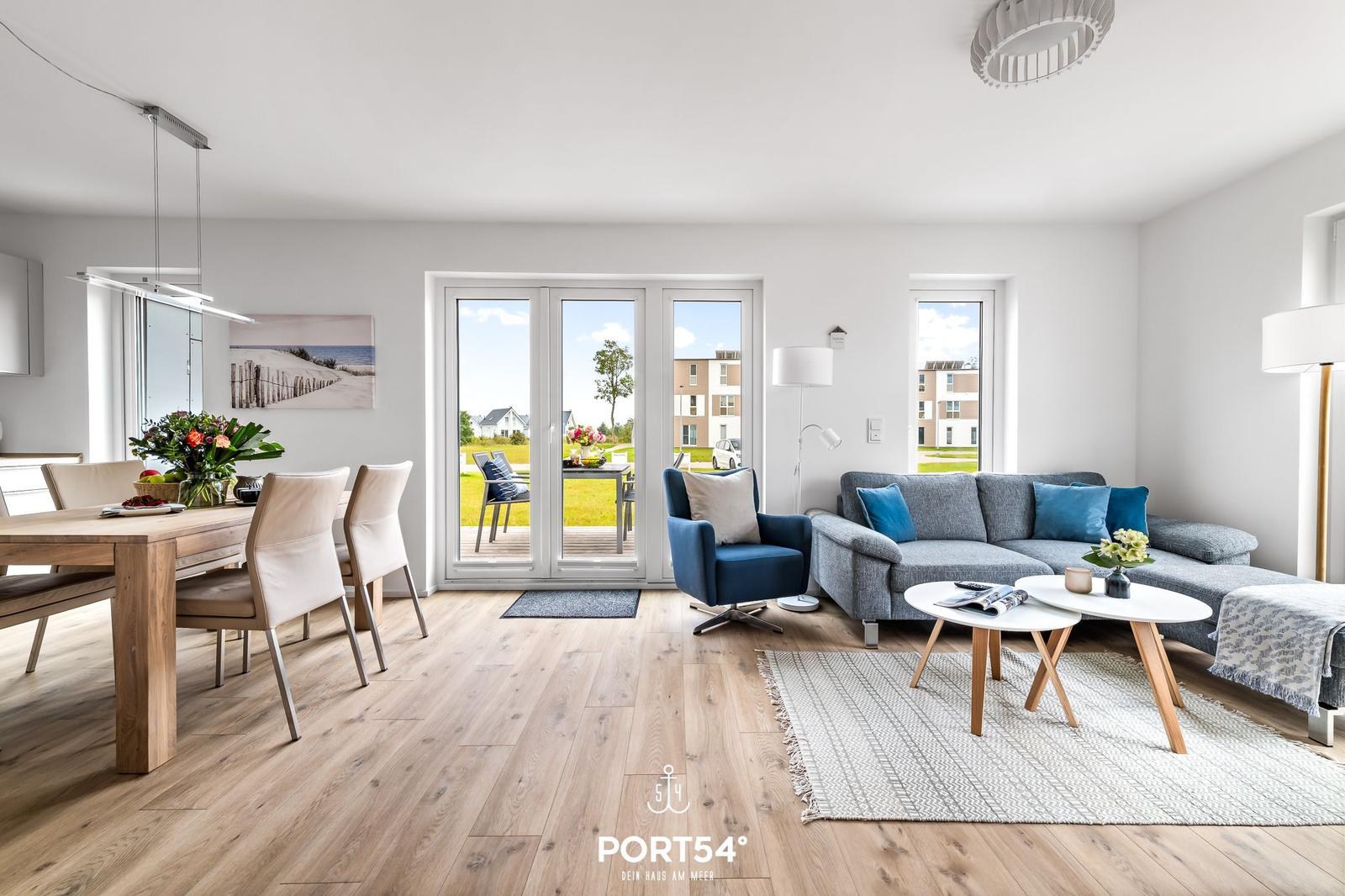 Wohn- und Essbereich mit Holzboden, Sofa, Stühlen und Blick auf den Garten.