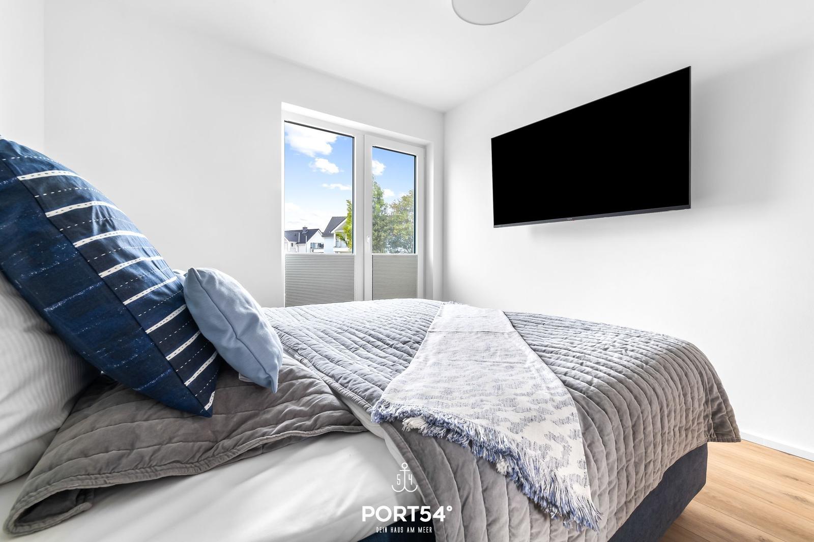 Schlafzimmer mit Bett, TV und Fensterblick auf Außenbereich.