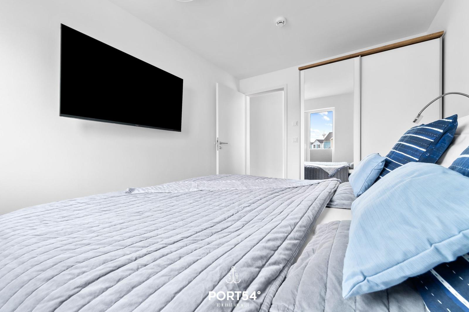 Schlafzimmer mit Bett, Fernseher und Schiebetüren. Blick auf Balkon.