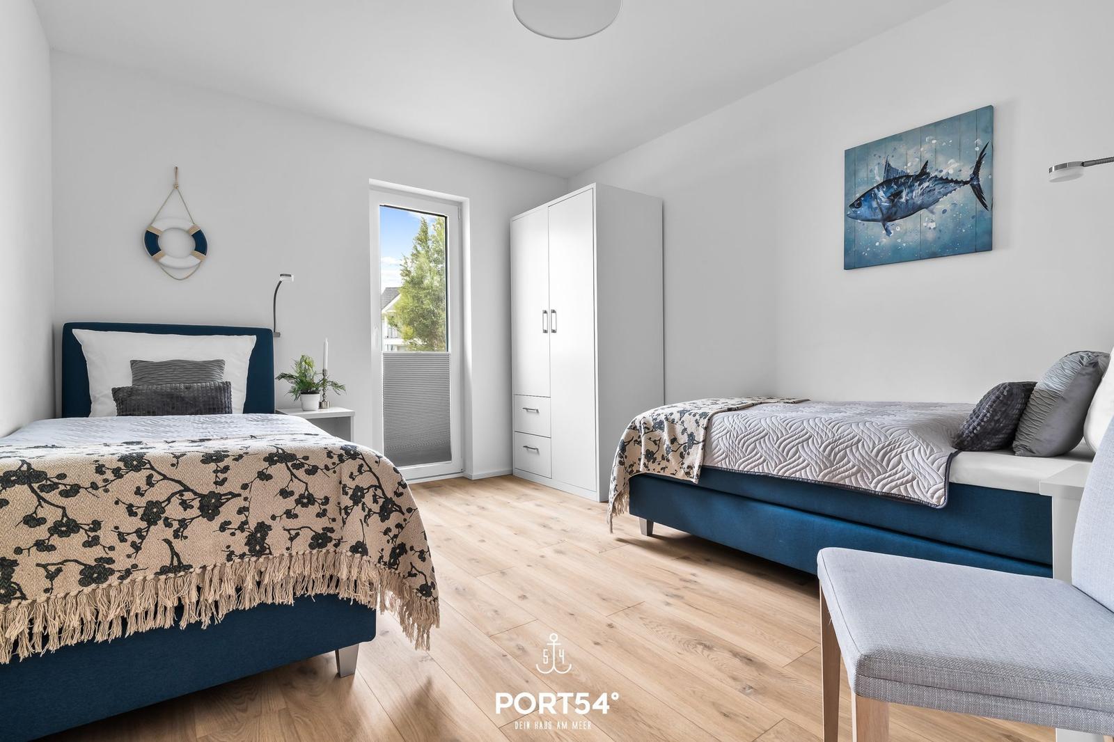 Zwei Betten mit blauen Kopfenden, weißer Kleiderschrank und Wandbild mit Fisch.